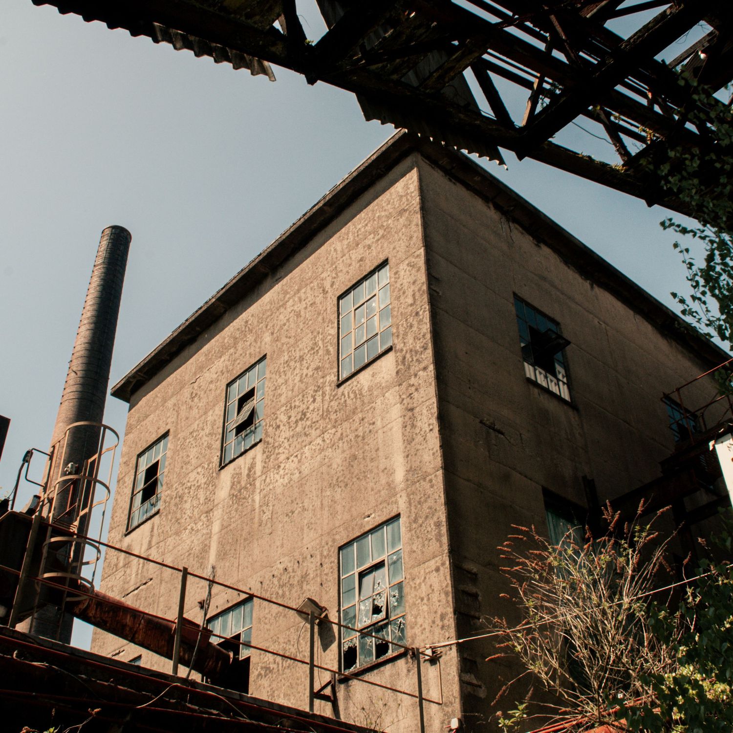 Exterior of derelict cwm coke works with metal cladding and narrow windows, viewed from below alongside pipes and scaffolding. ash olion