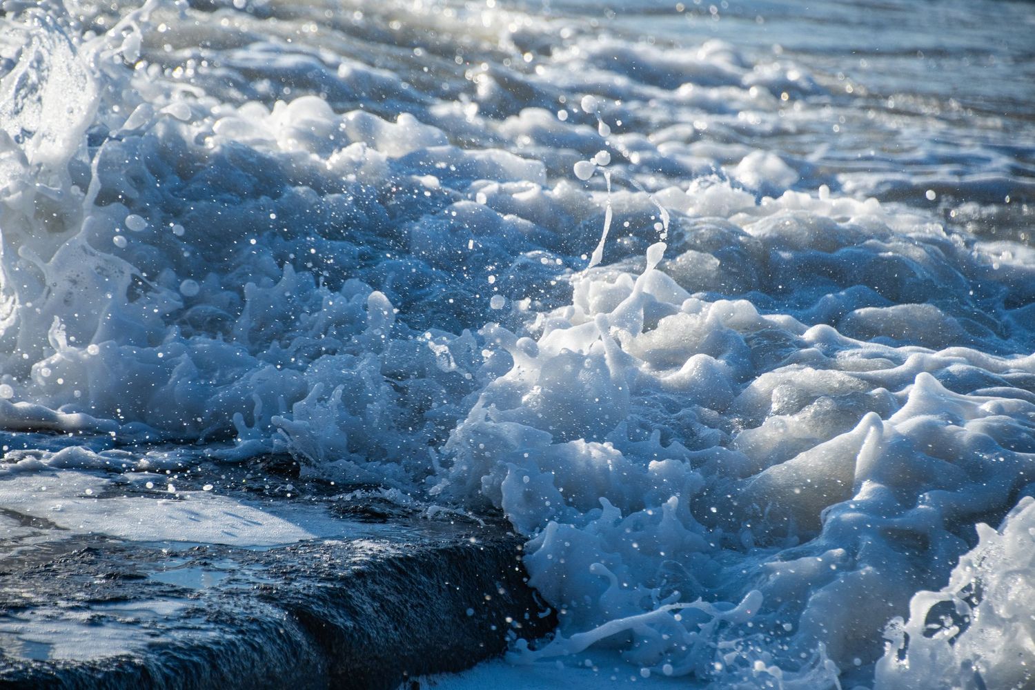 Close-up of churning ocean waves and white sea foam crashing over dark rocks. ash olion photography. nature, ocean, fine art photography
