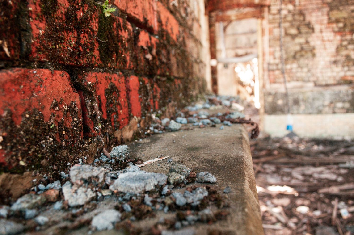 Low-angle close-up of a crumbling brick wall with scattered rubble and peeling paint in an abandoned building