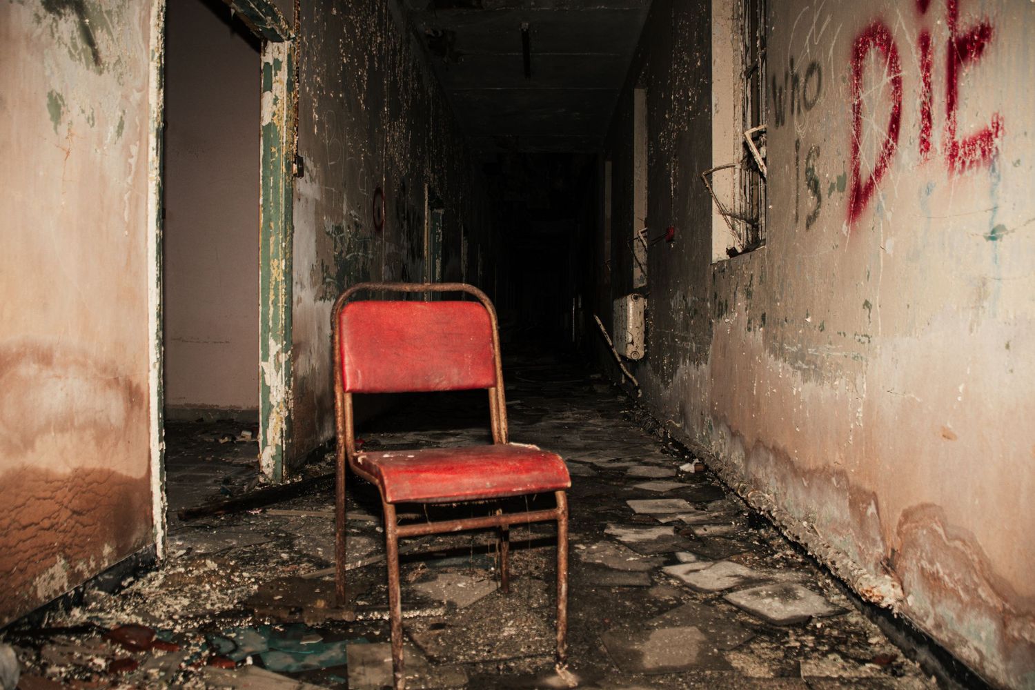 Single red chair placed in the middle of a decaying corridor, with cracked floors, peeling walls, amman valley maternity hospital