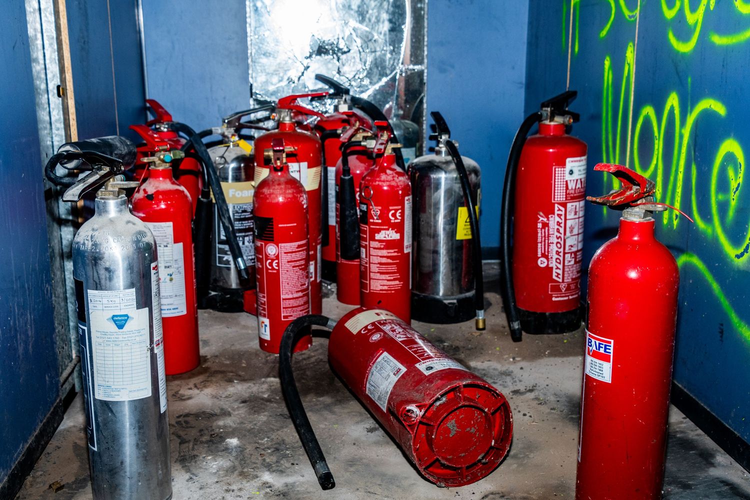 Group of red and silver fire extinguishers scattered across the floor of an abandoned, graffiti-covered room. ash olion photo. spin bowling