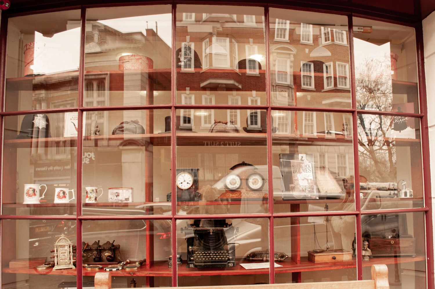 Large grid-framed window showing a display of vintage objects inside, while the exterior buildings are reflected across the glass. ash olion