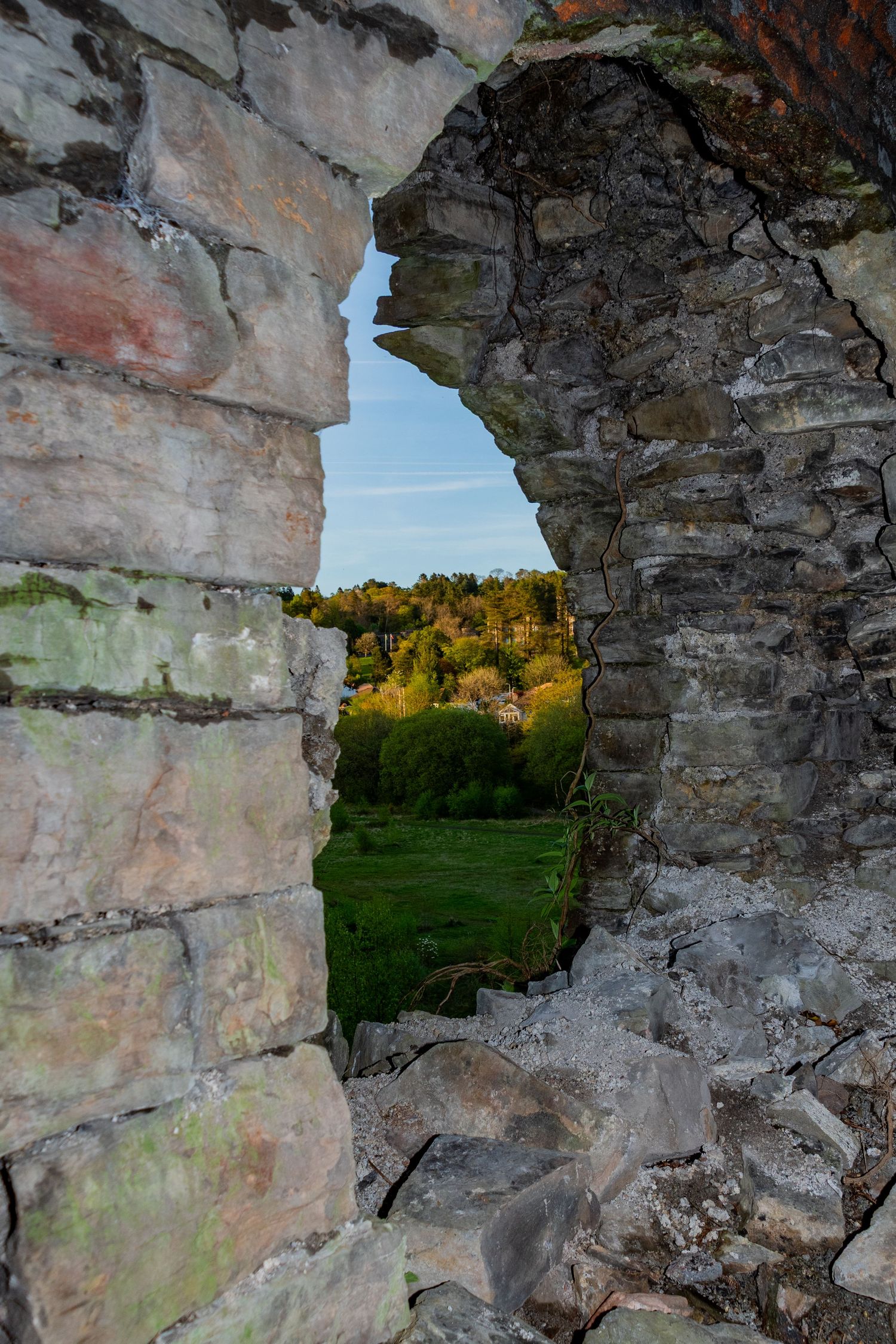 Weathered stone archway from an ancient ruin, looking out toward a sunlit landscape beyond. merthyr ironworks. welsh industry and coalfield.