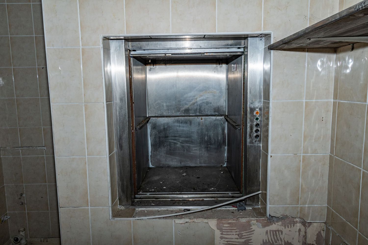 Old stainless-steel service lift with tarnished metal doors set in tiled walls of an abandoned building. spin bowling cardiff. urbex abandon