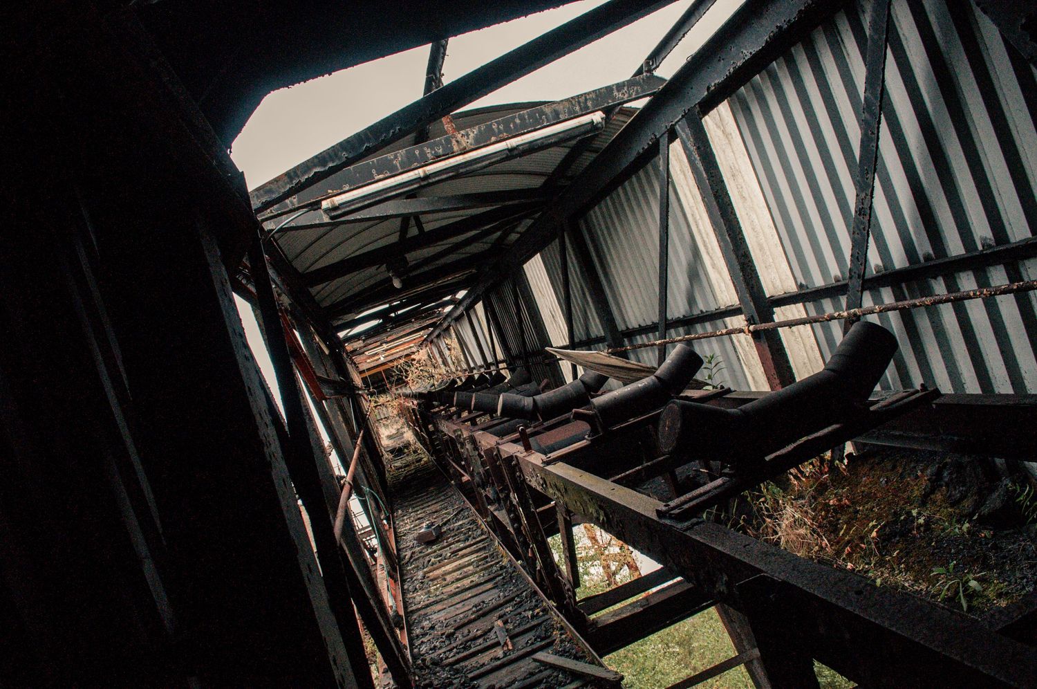 Interior of a decaying coal conveyor with rusted beams and shattered roofing, leading into darkness. cwm coke works ash olion
