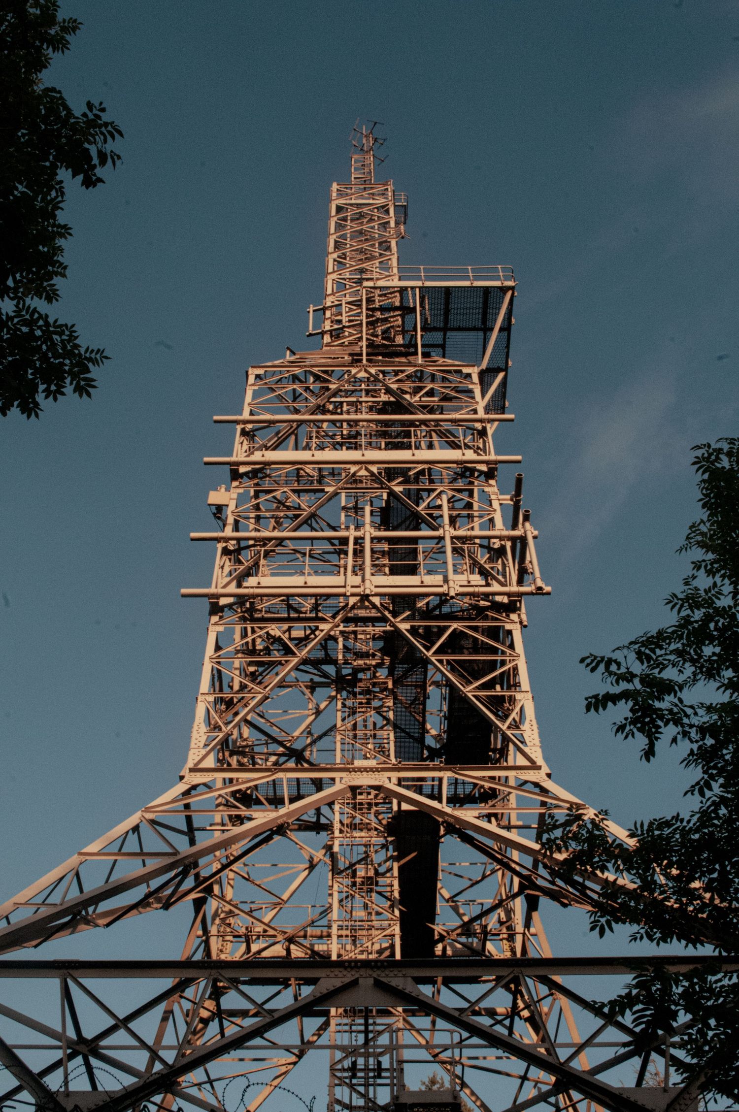Ash Olion Wales Tall steel industrial tower photographed from below, its lattice framework glowing in warm light against a blue sky,