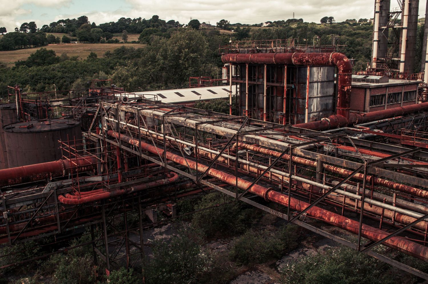 Wide view of a decaying industrial plant with rusted pipes and structures sprawling across a landscape slowly being overtaken cwm coke works