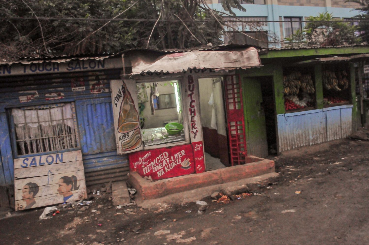 Weathered roadside shop with peeling paint, hand-painted signs, and goods displayed behind metal bars. Kenya, Africa