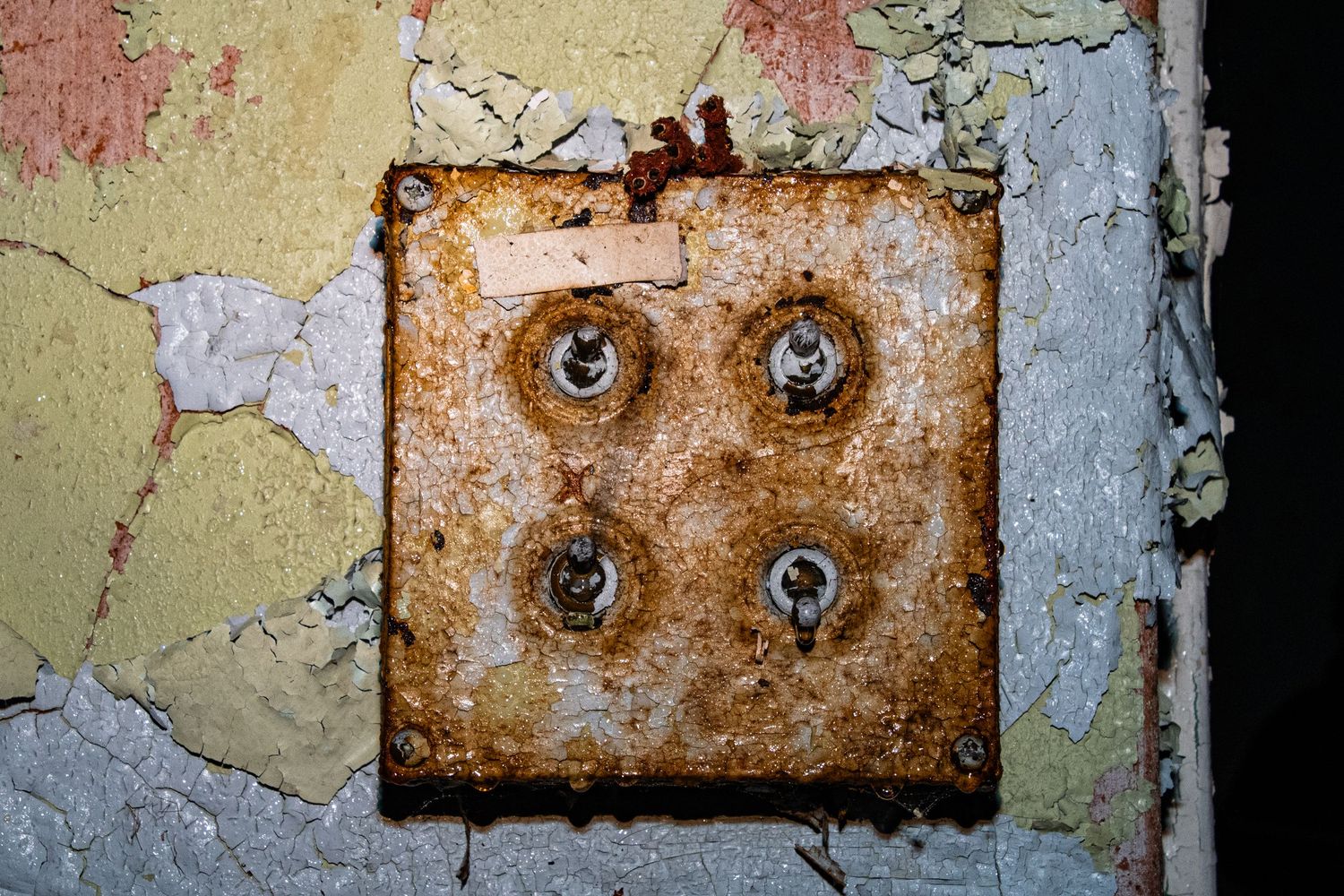 Close-up of a heavily rusted electrical switch panel mounted on cracked, flaking paint. amman valley maternity hospital ash olion photo