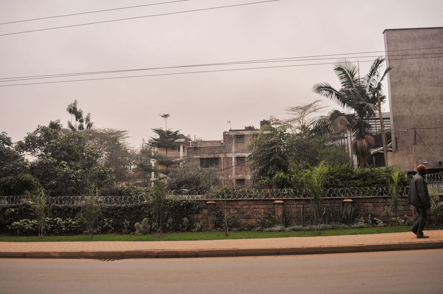 Row of residential buildings partly hidden behind tall trees and greenery, seen from across a main road. Kenya, Africa