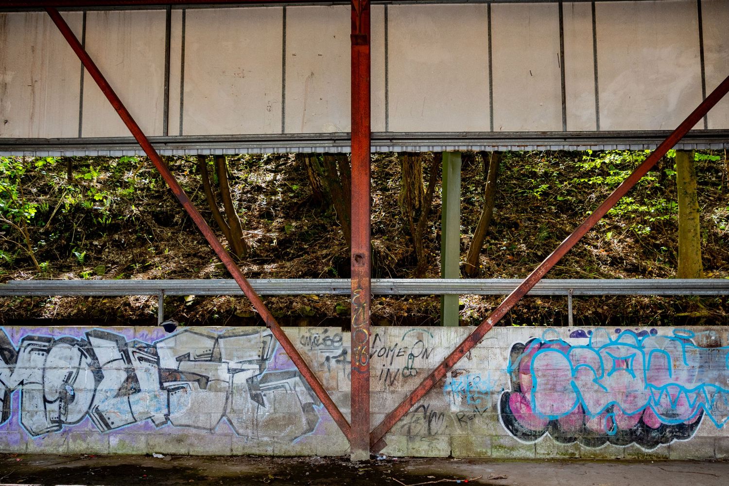 Rusted steel support beams inside an abandoned industrial structure, with graffiti covering the concrete wall beneath. welsh coalfield.
