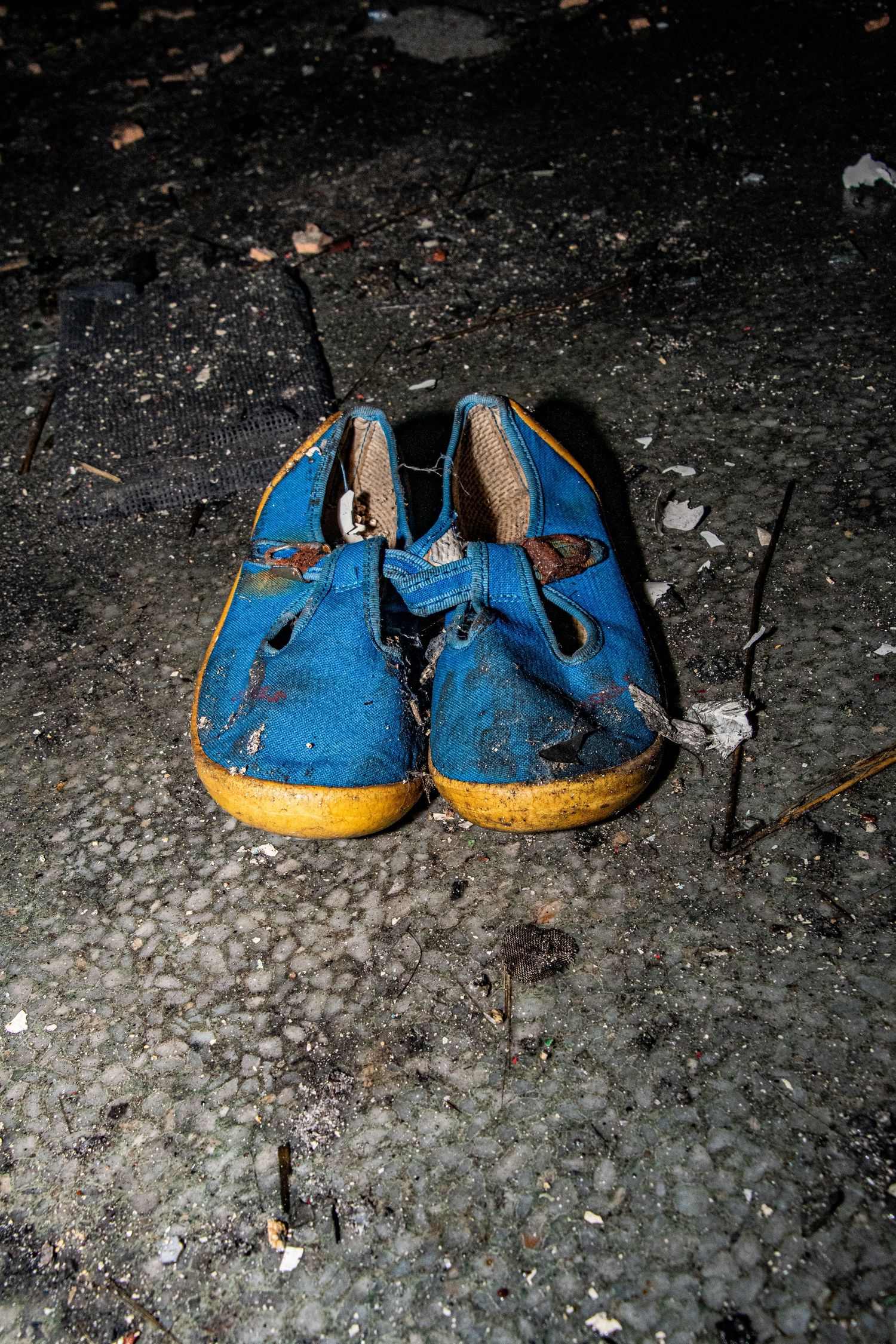 Pair of worn blue child's shoes abandoned on a dusty, debris-covered floor inside an abandoned hospital. amman valley hospital ash olion