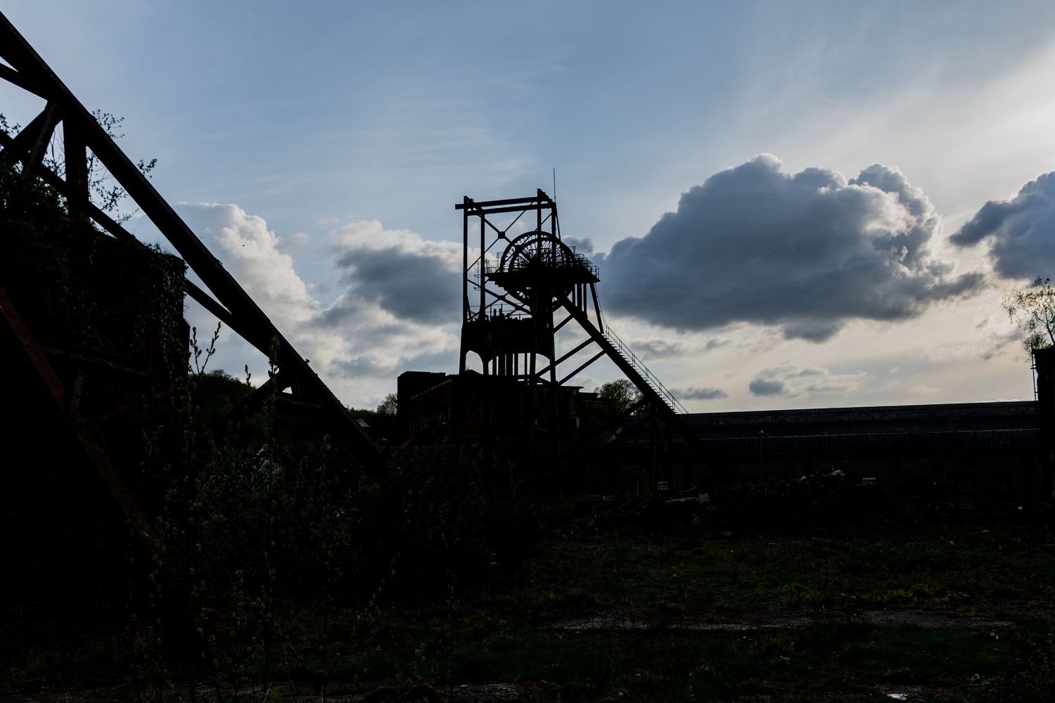 Silhouetted mining headframe against a bright evening sky with dramatic clouds.  penallta colliery. ash olion photography. derelict wales