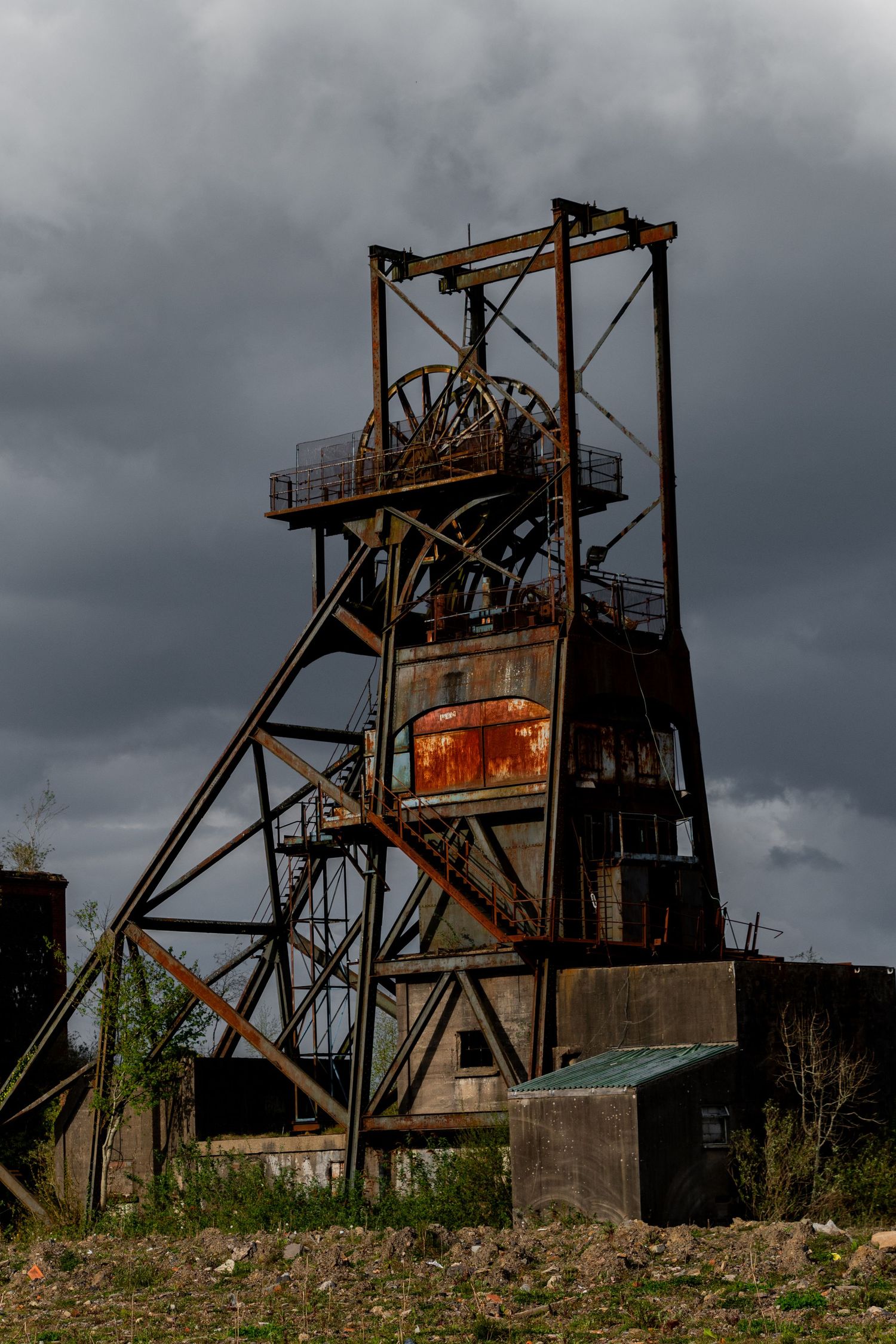 Tall abandoned mining headframe silhouetted against a dark cloudy sky, with rusted machinery visible at its centre.  penallta colliery