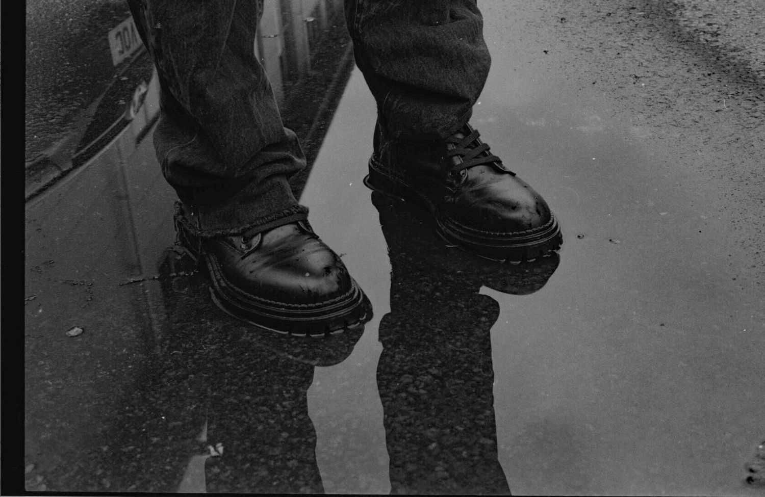 35mm traditional film photography, boots reflected in water. person is crisply reflected in the puddle. fine art photogrpahy by ash olion
