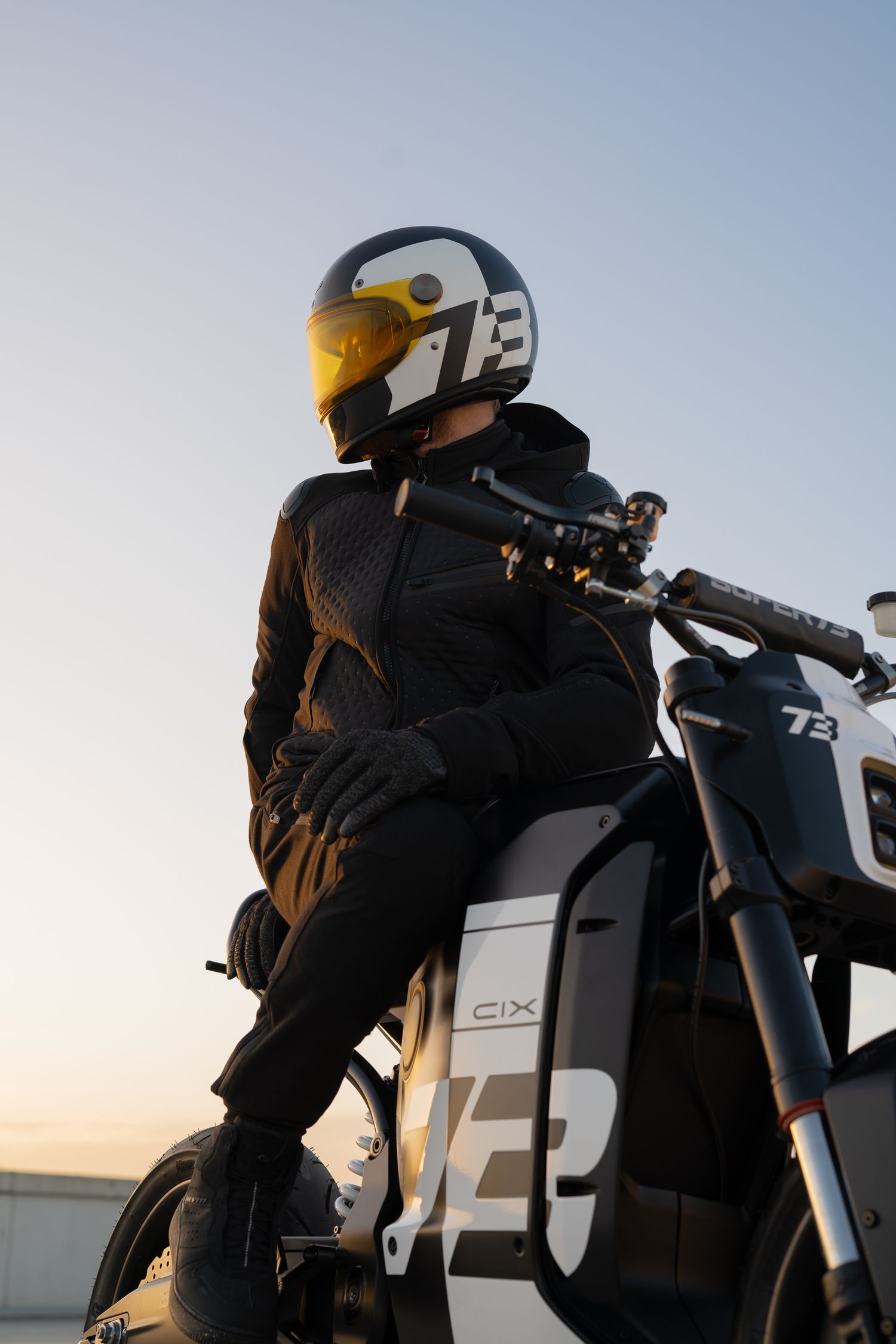 Motorcyclist in black gear riding a sleek motorcycle against a sunset sky.