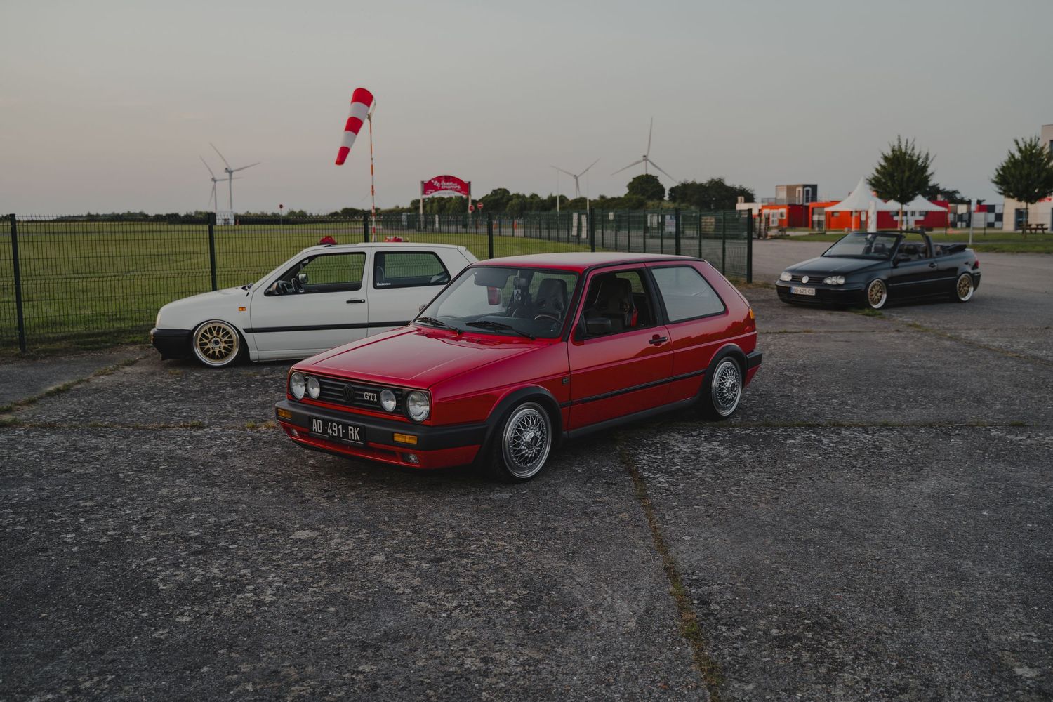 Classic red and silver Volkswagen cars parked at dusk with a windsock visible in the background.