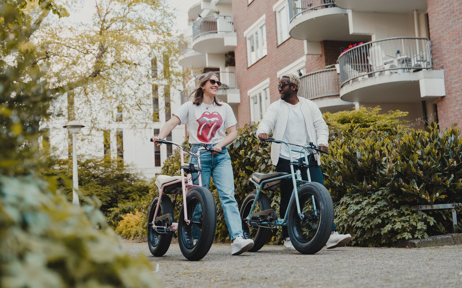 Motorcycles lined up outside brick residential building with autumn foliage.