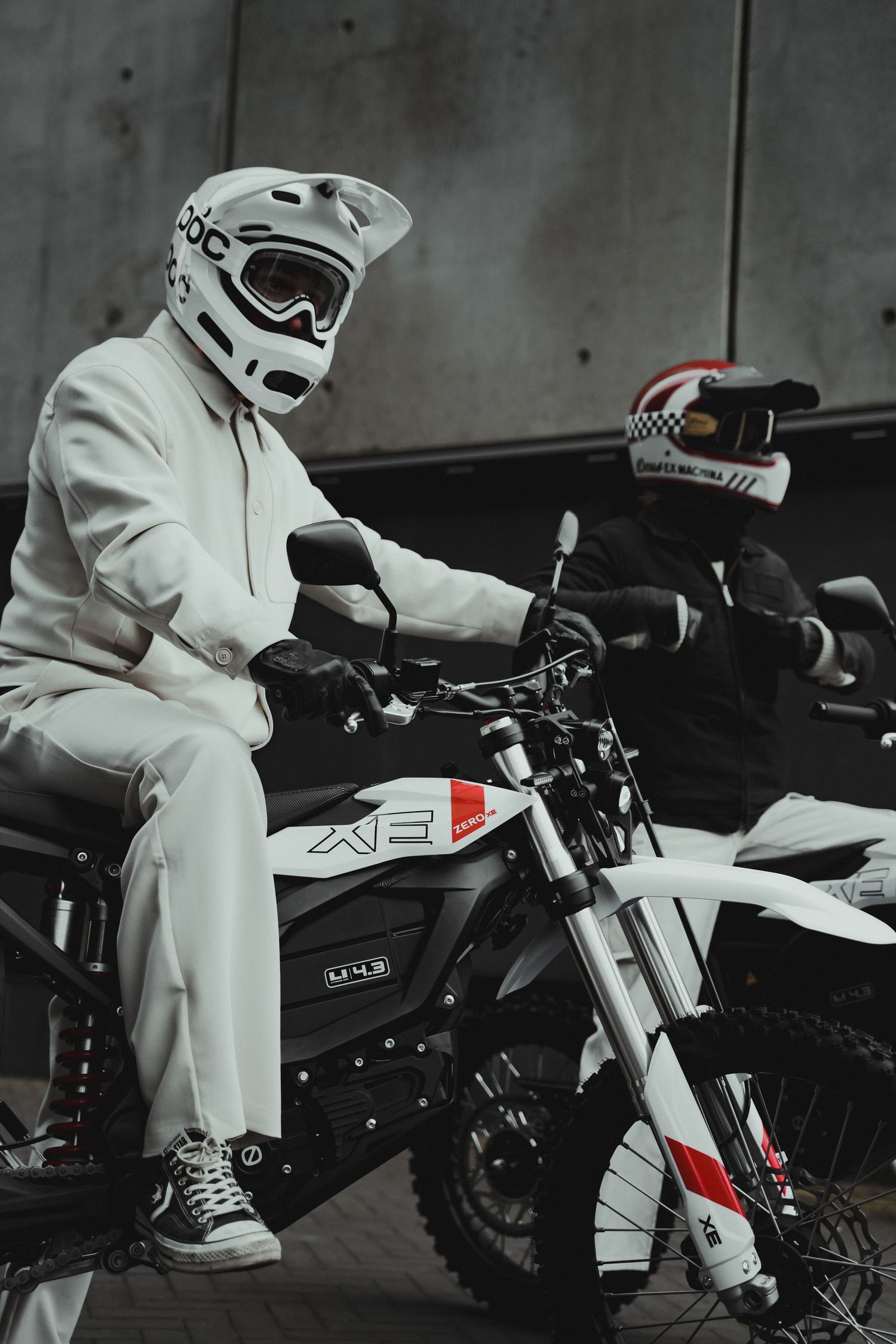 White-clad rider seated on a modern dirt bike in a dark industrial setting.