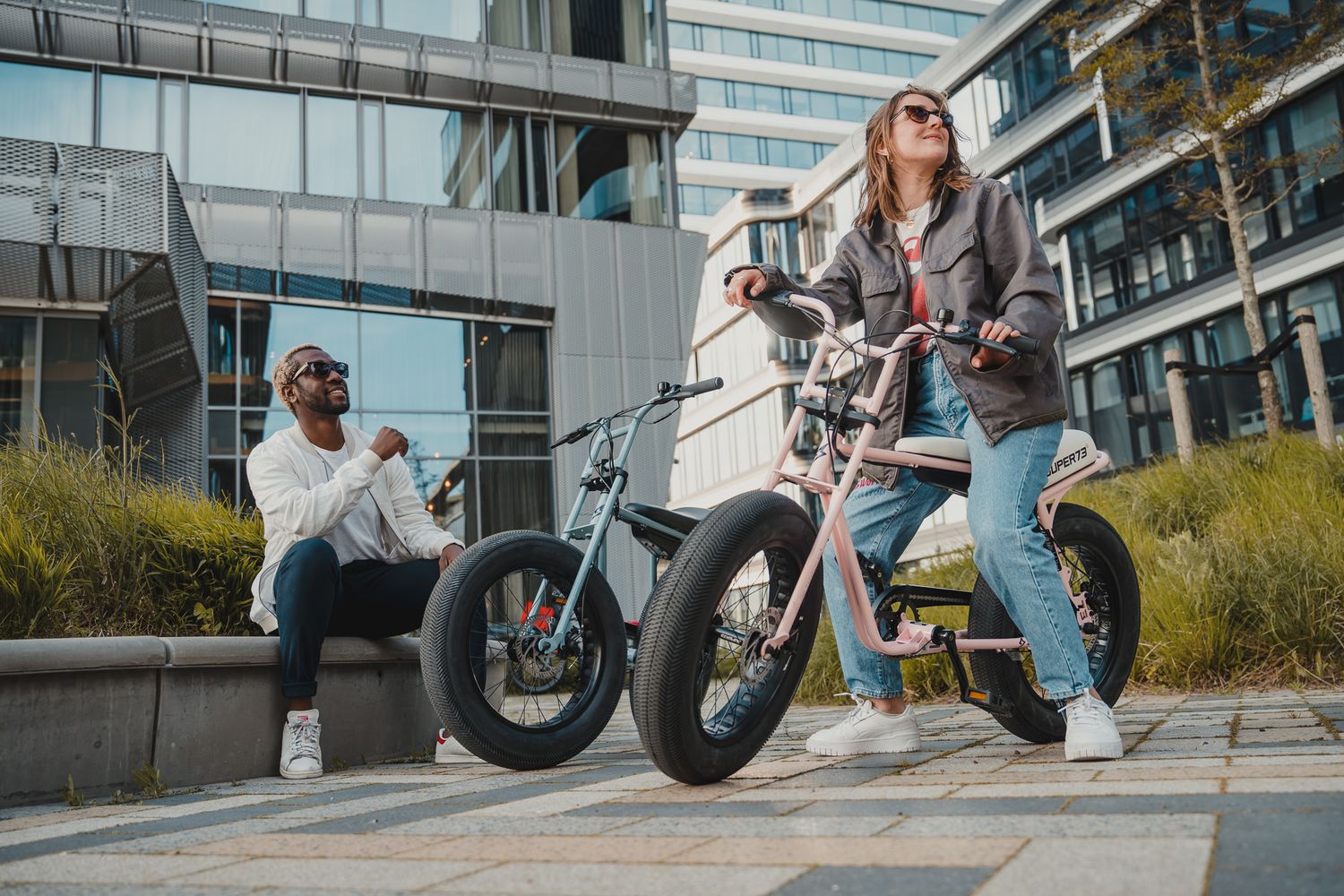 Electric bike rider performs trick maneuvers in an urban setting with modern buildings in background.
