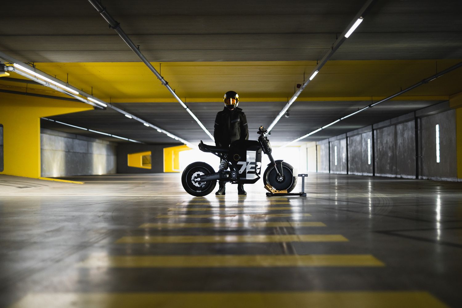 Dramatic low-angle view of motorcycle in underground parking garage with yellow ceiling.