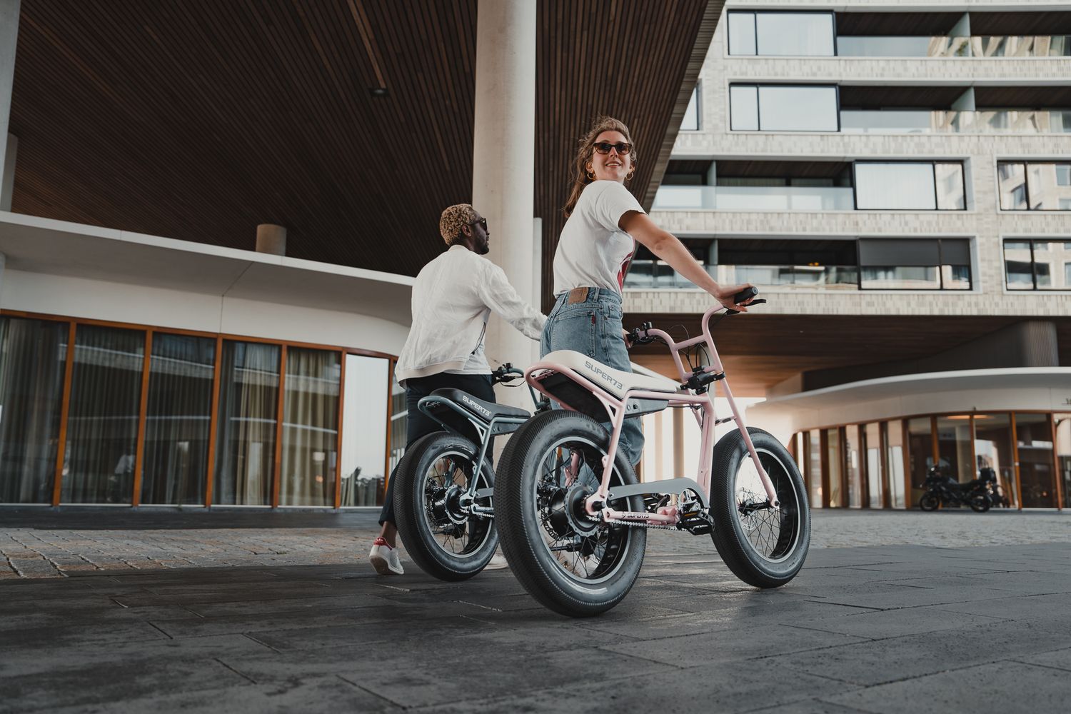 People riding motorcycles in an urban setting with modern architecture.