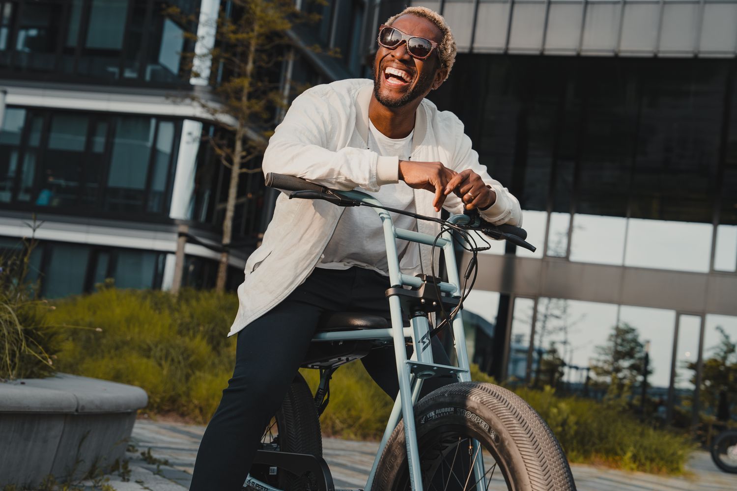Person riding an electric bike demonstrates stunts against modern architectural backdrop.