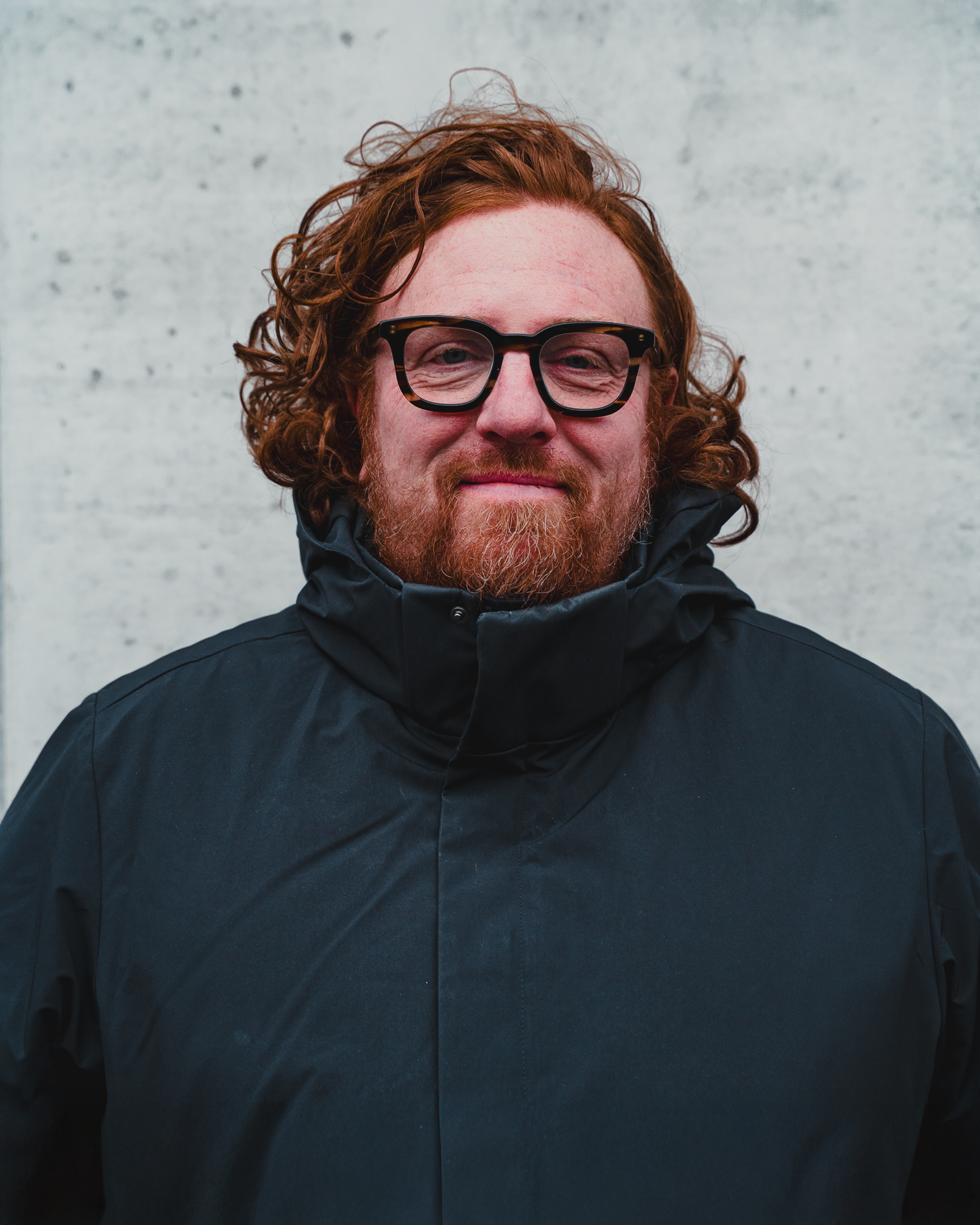 Portrait series showing person in dark jacket wearing glasses with red beard.