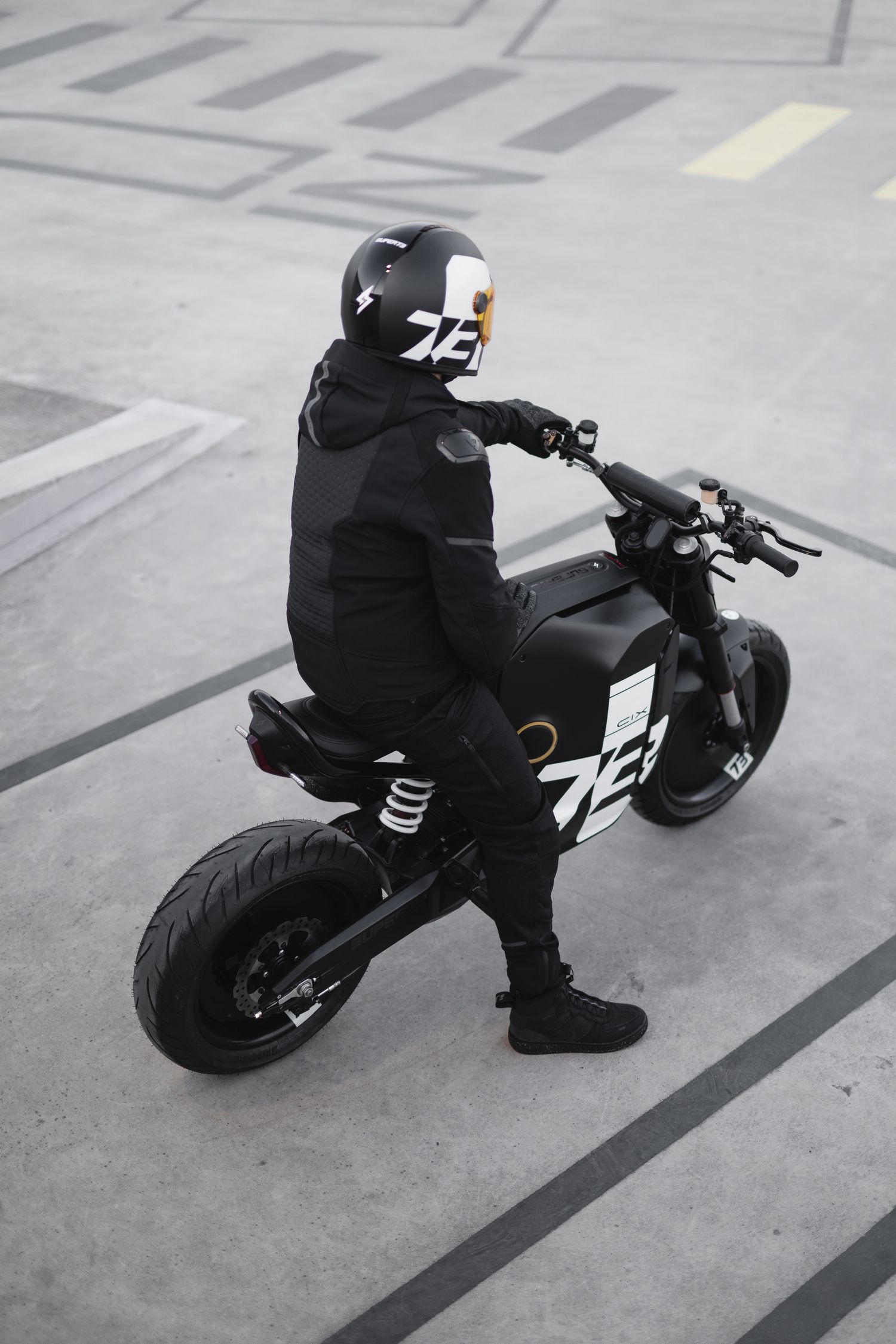 Rider crouched on parked black motorcycle on concrete surface.