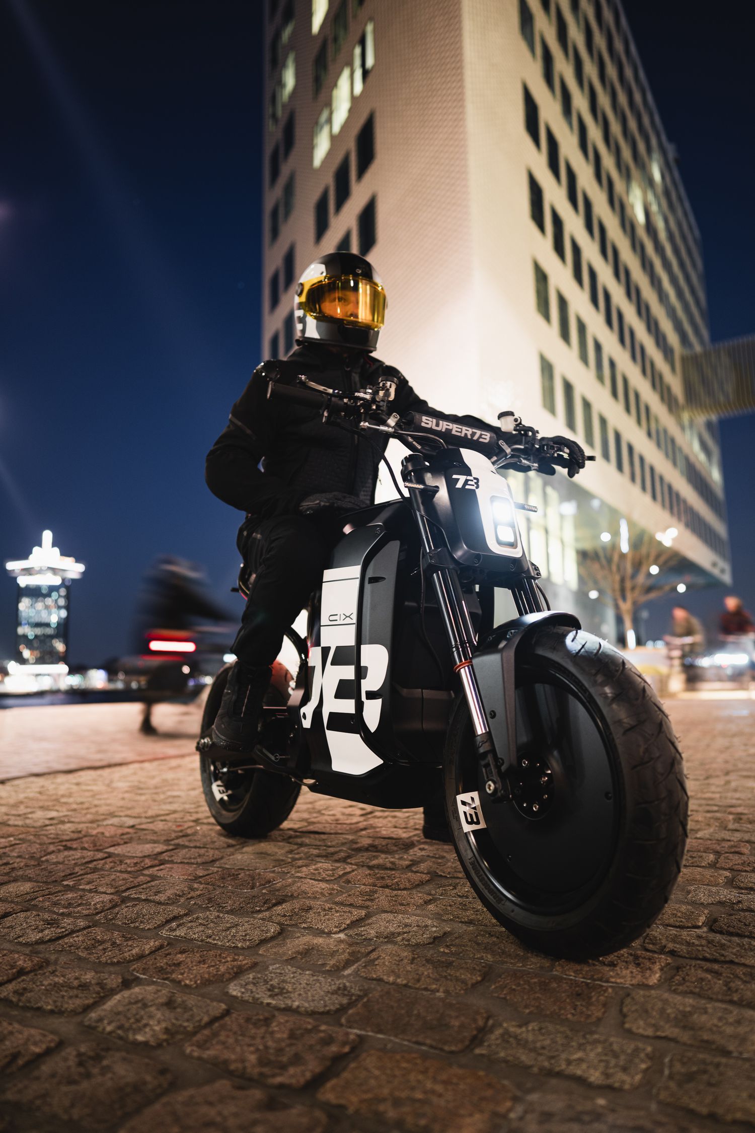 Black motorcycle illuminated at night against urban building backdrop.