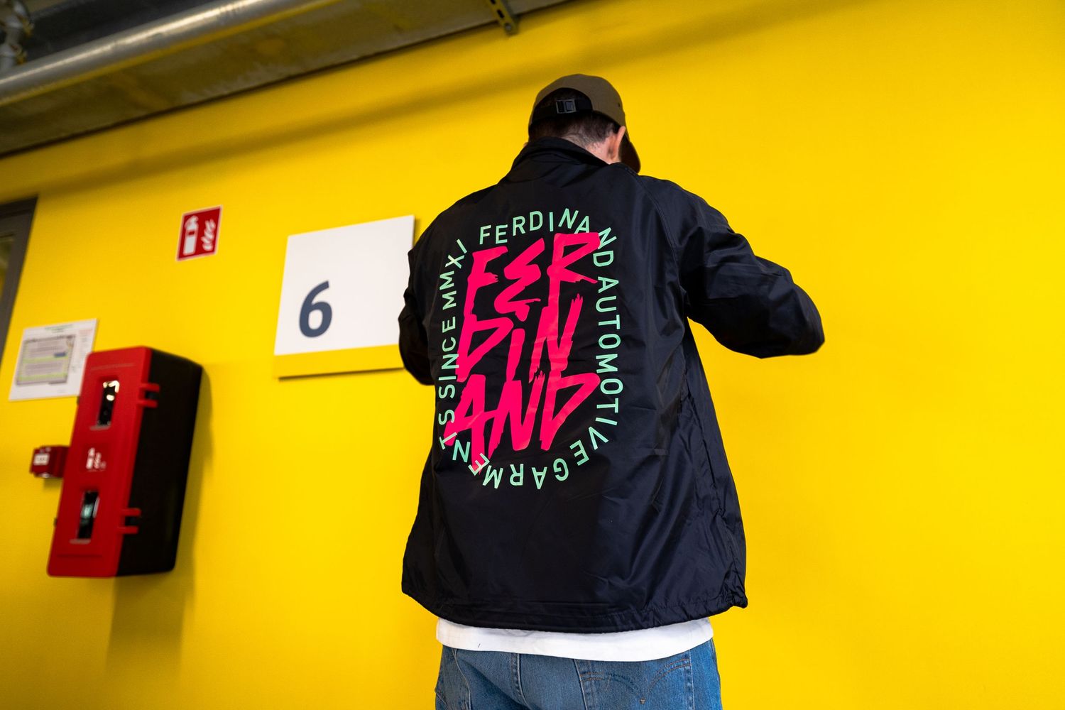 Black jackets with pink text displayed against vibrant yellow wall.