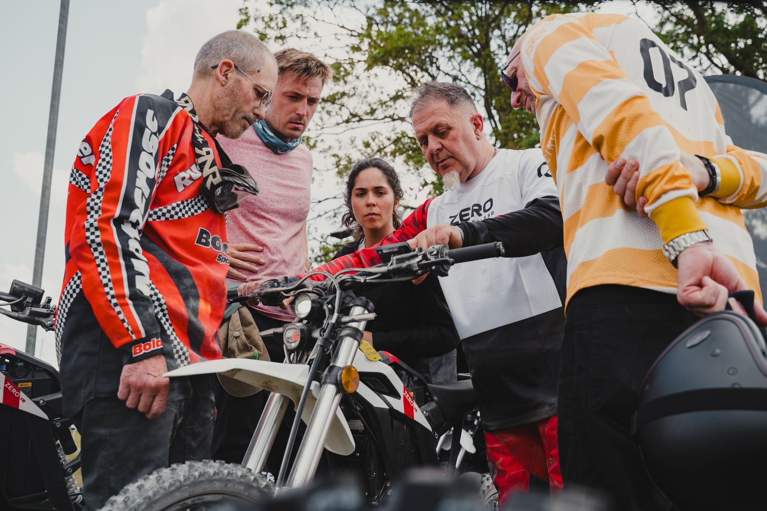 Group of motorcycle enthusiasts gathered around bikes at an outdoor event.