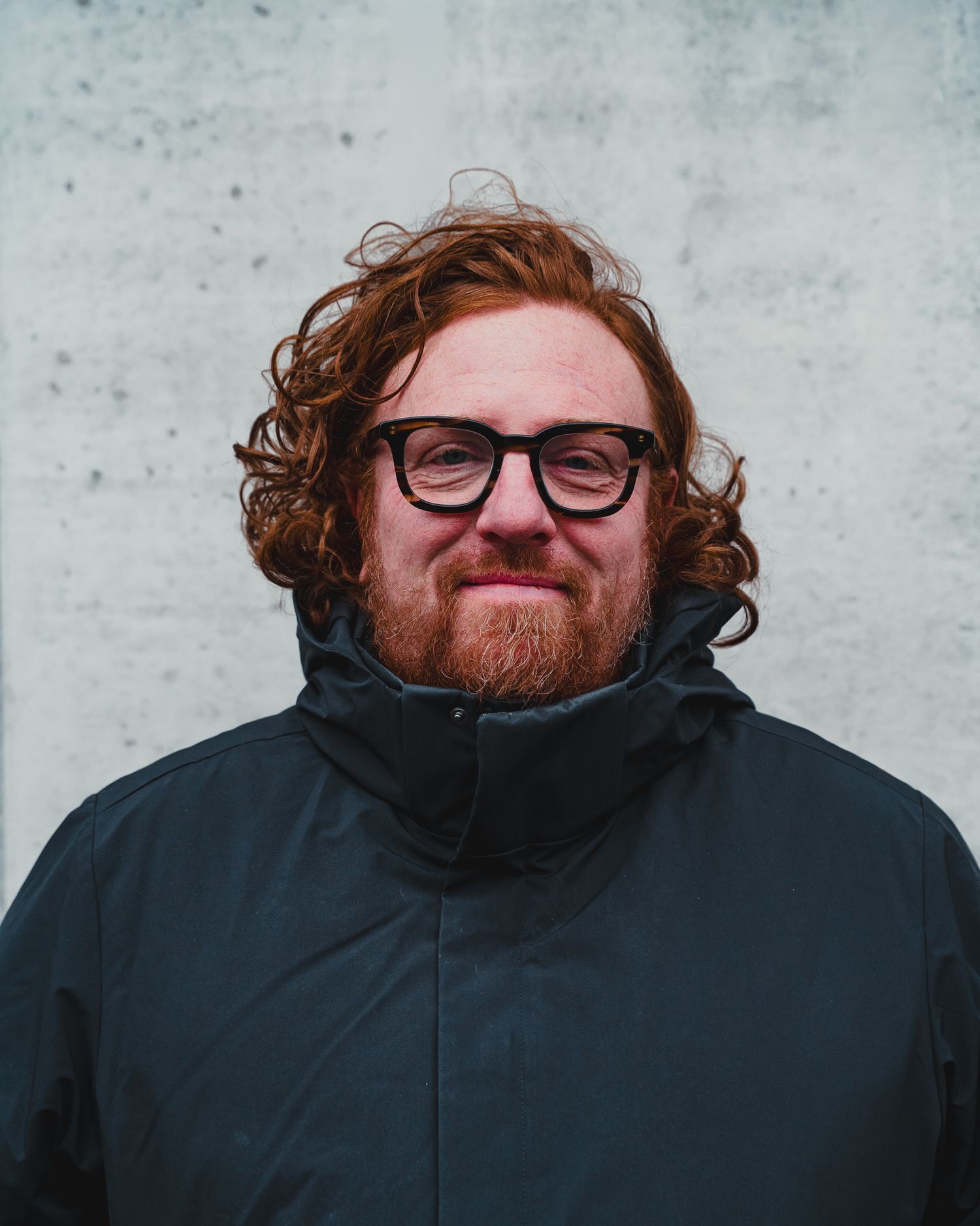 Multiple headshots of person wearing glasses and black jacket against grey wall.