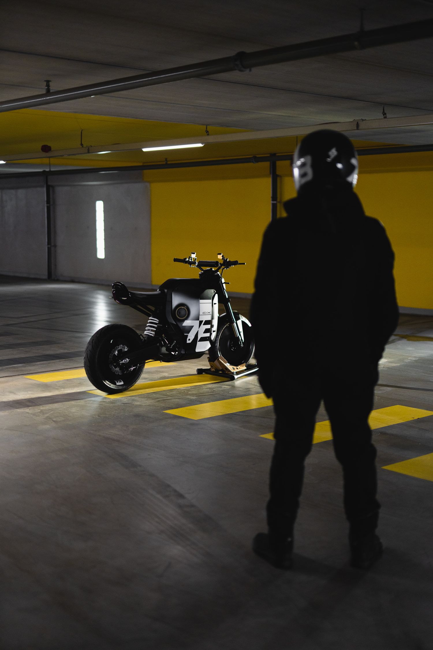 Black motorcycle parked in dimly lit underground parking garage with yellow markings on floor.