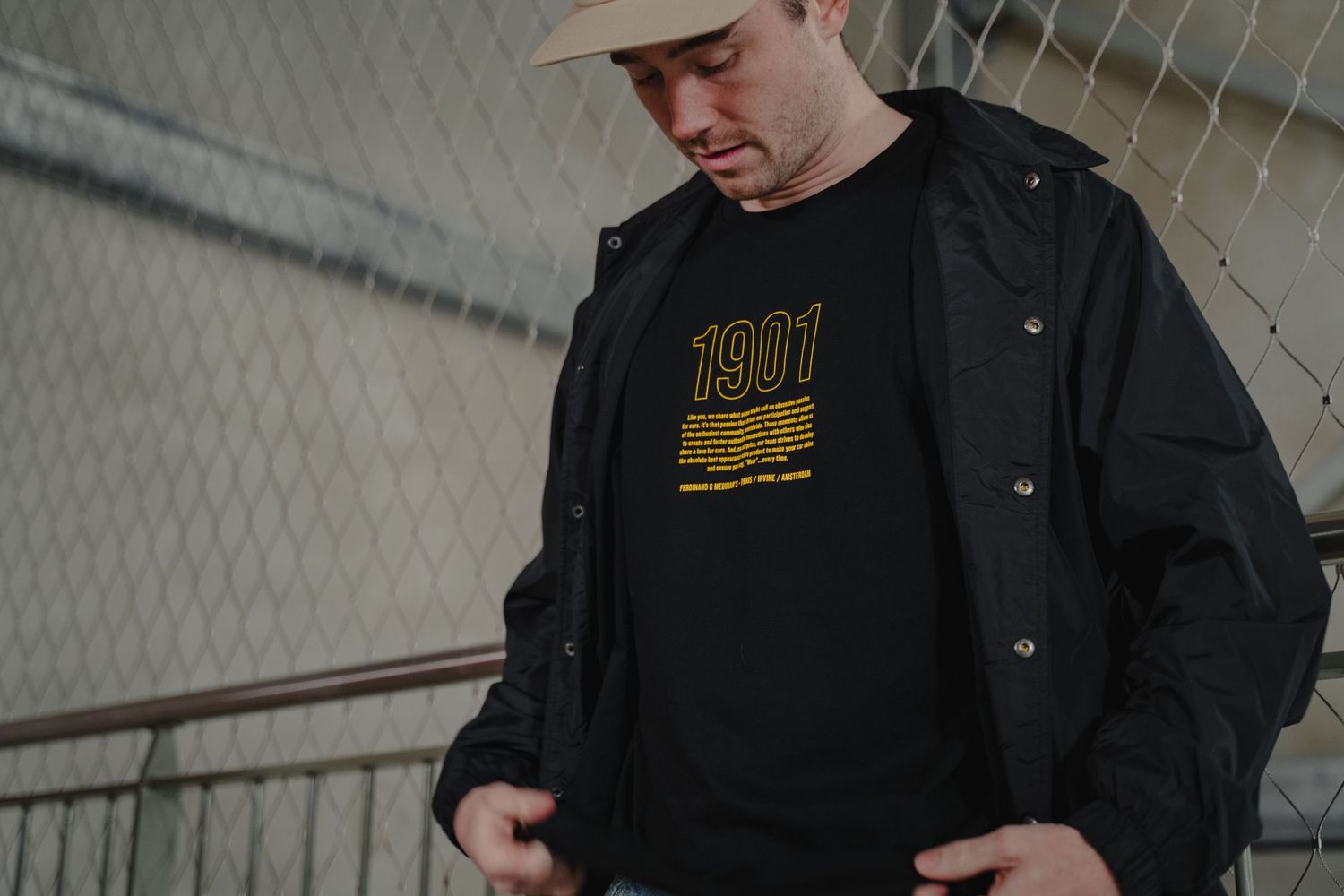 Person wearing baseball cap and black jacket in industrial setting.