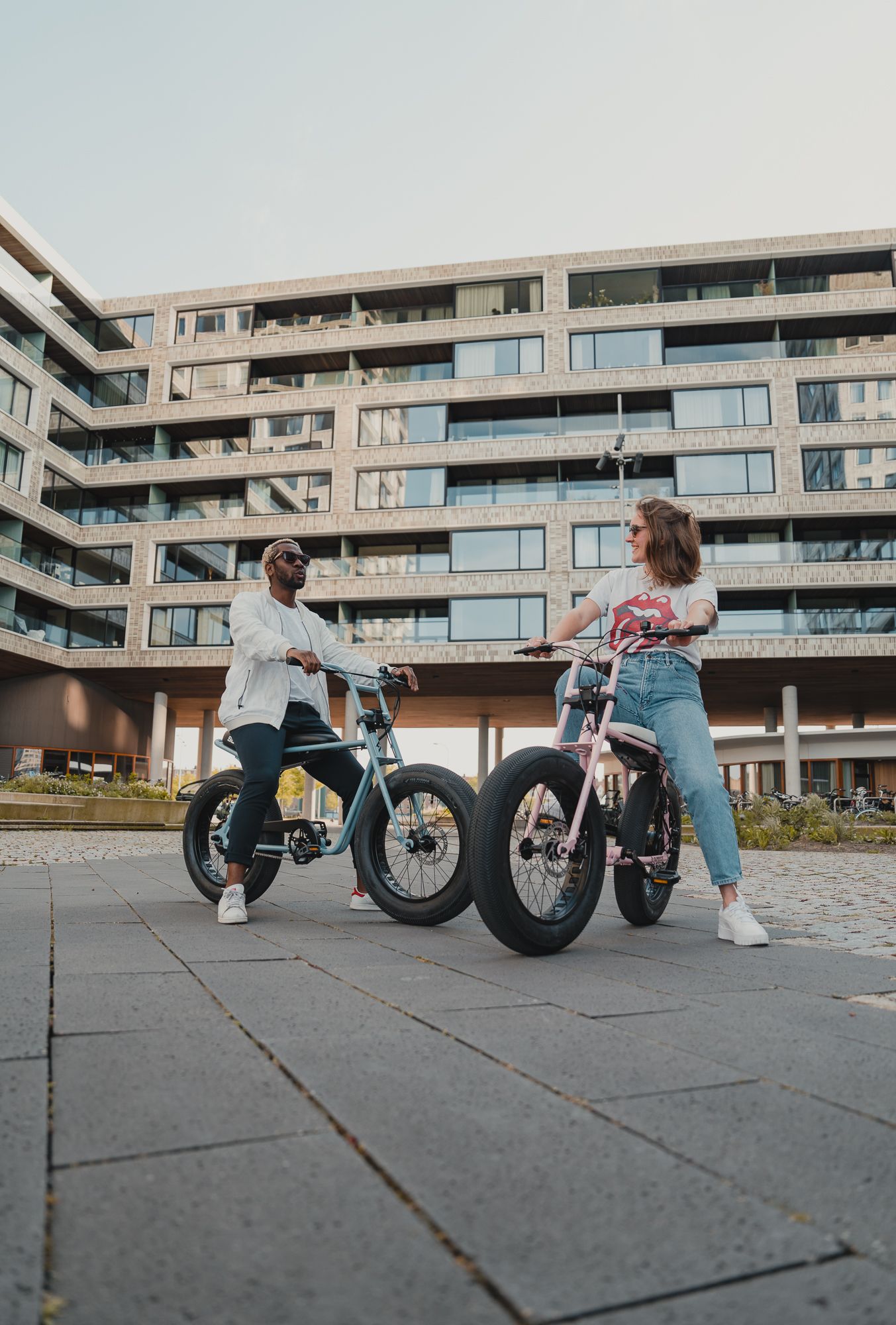 Electric bikes lined up on concrete pavement with modern apartment complex in background.