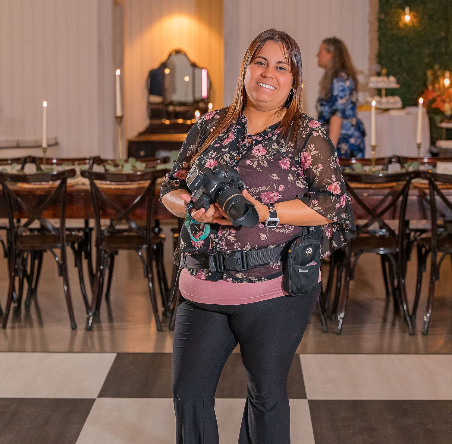 Woman in a pink top and jeans showing off her outfit in a rustic venue with wooden chairs and warm lighting.