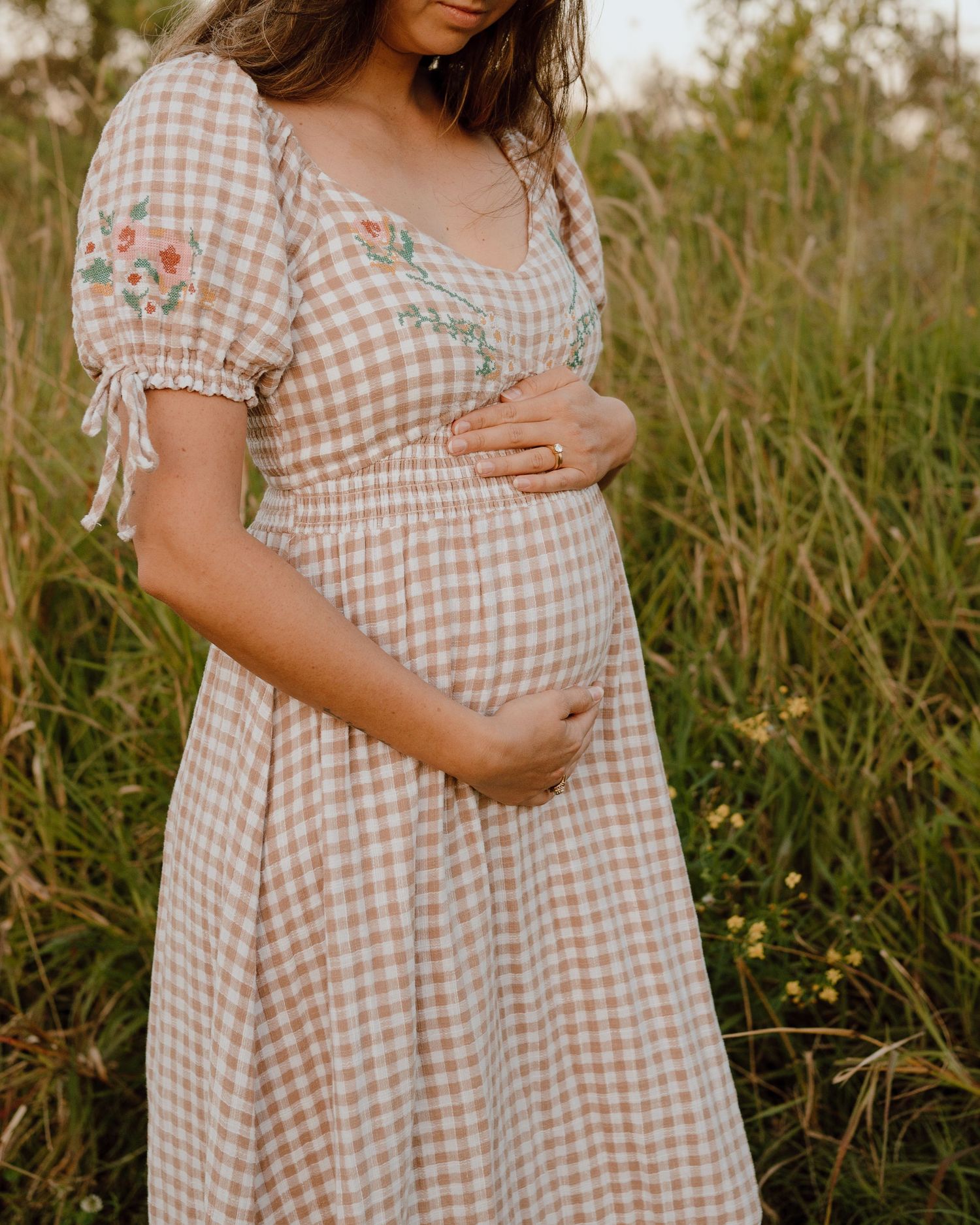 Close-up of pregnant woman's belly in checkered dress against natural backdrop.