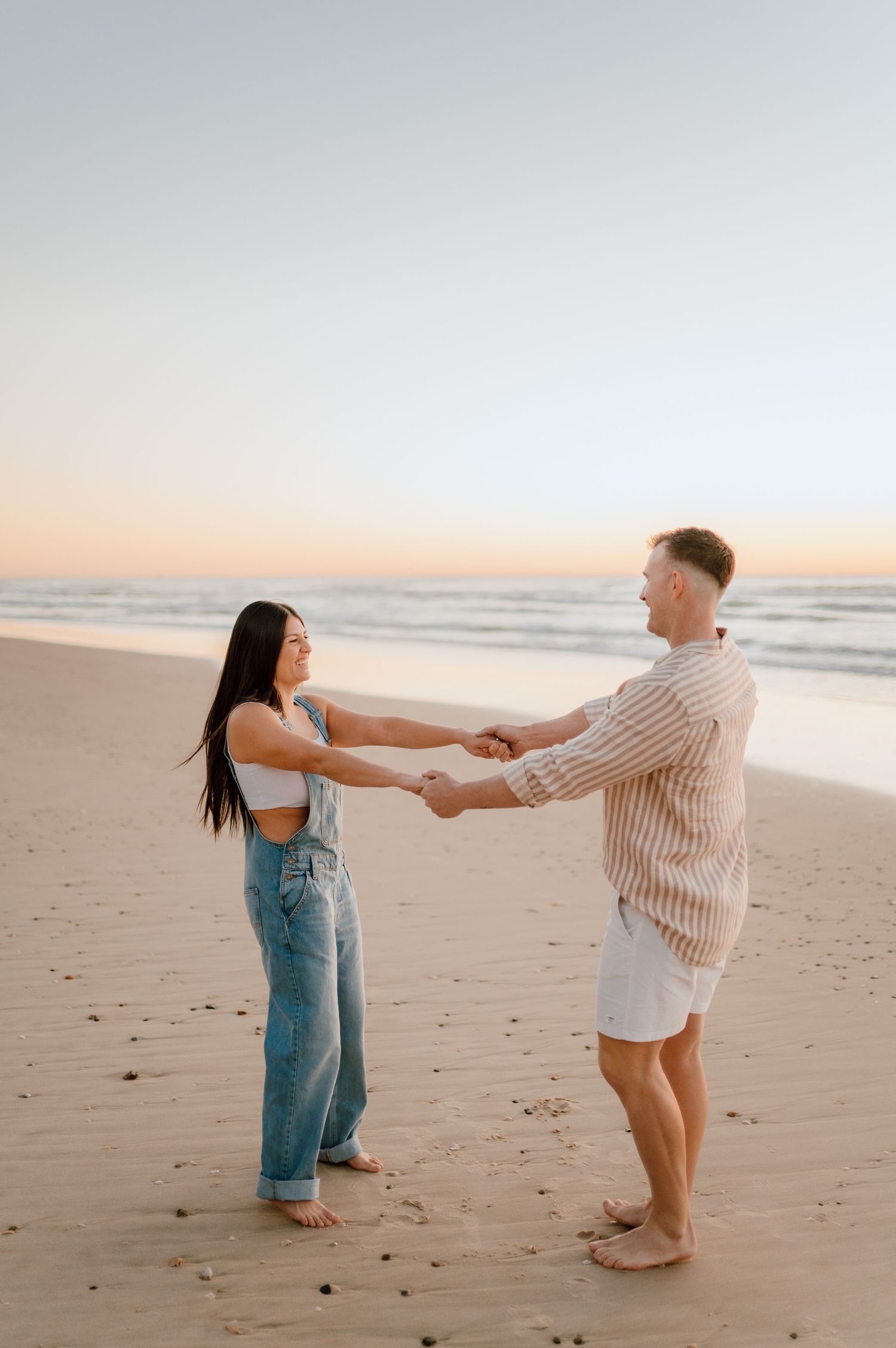 Playful couple dancing together on sandy beach at sunset.