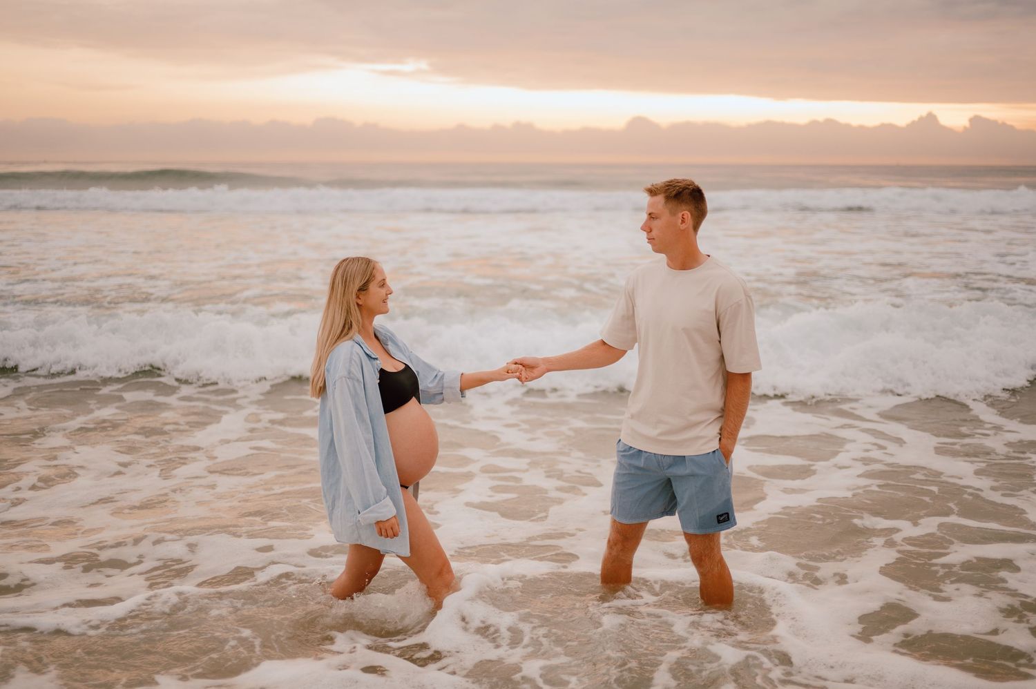 Two people playfully splash and chase each other along a sunset beach with waves crashing at their feet.