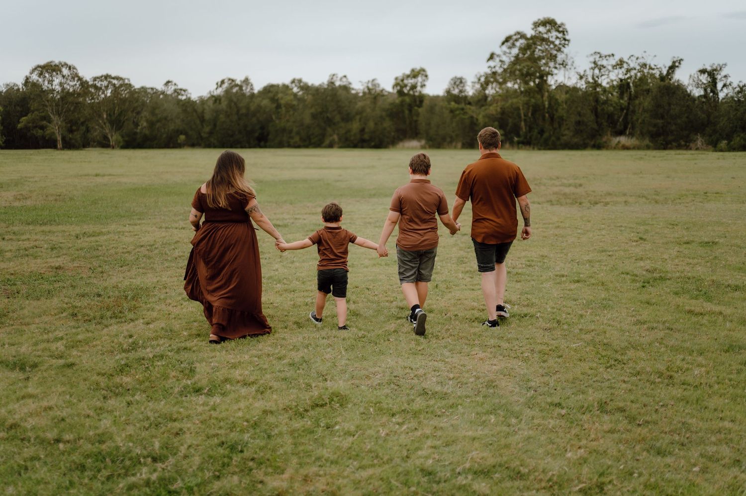 Family walking hand in hand through grassy field during sunset.
