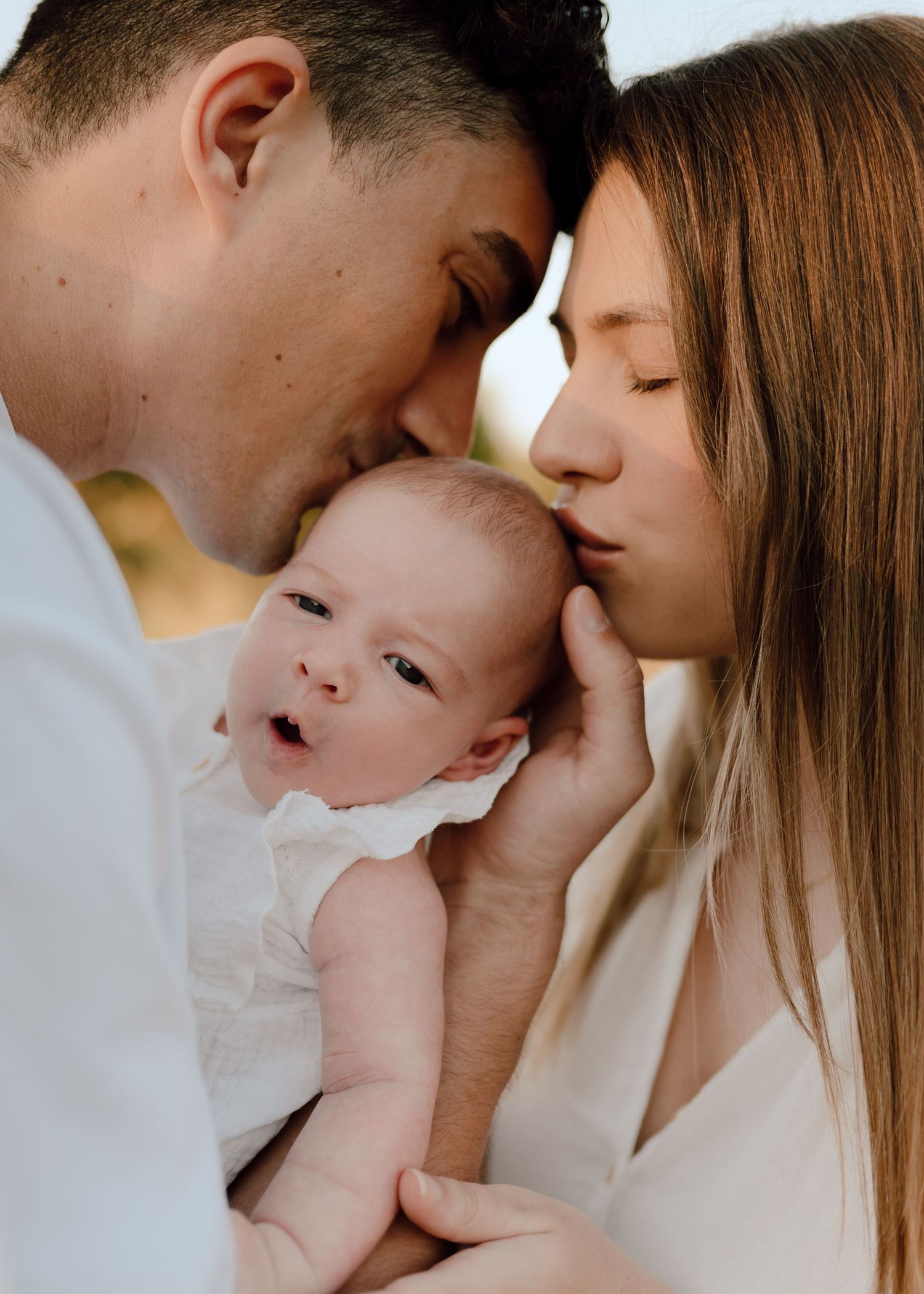 Intimate family moment with parents sharing tender kisses with their baby.