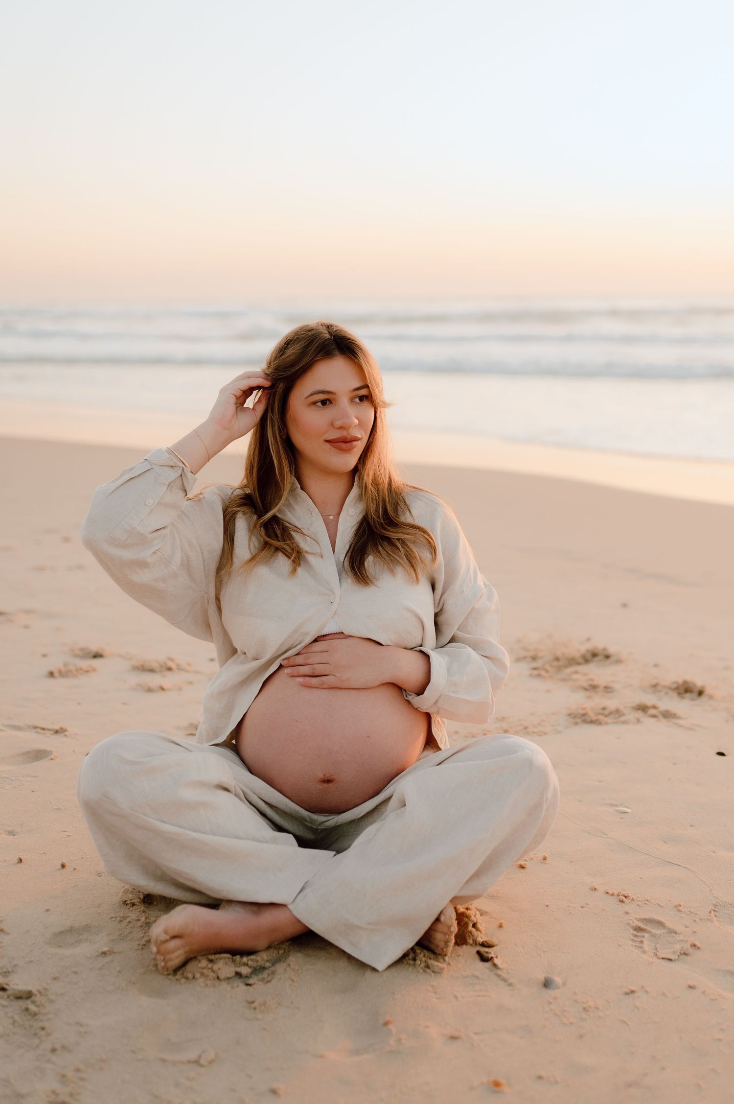 Artistic maternity session featuring white clothing against warm beach tones during golden hour.