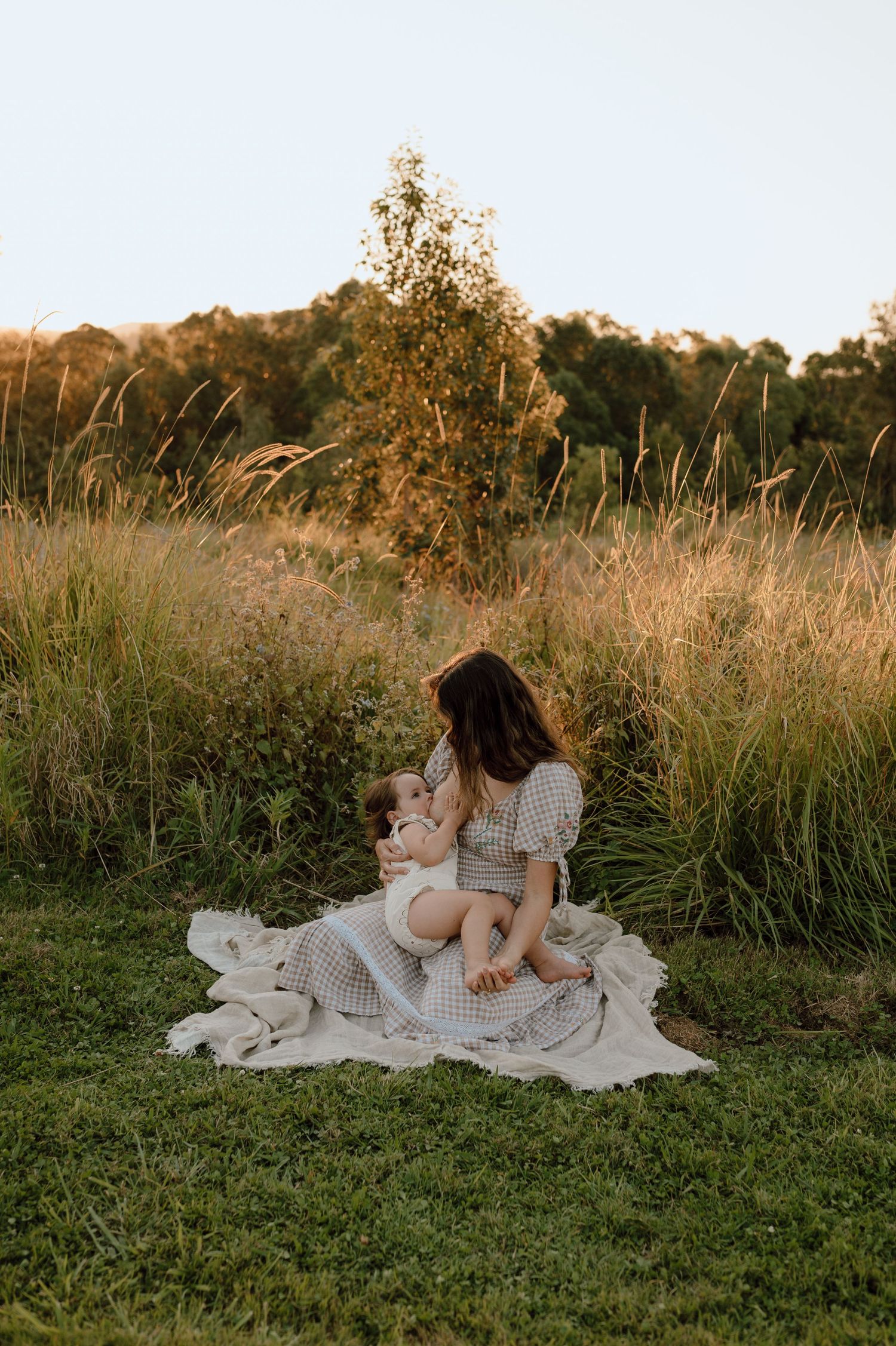 Family resting on blanket in grassy field during golden hour.