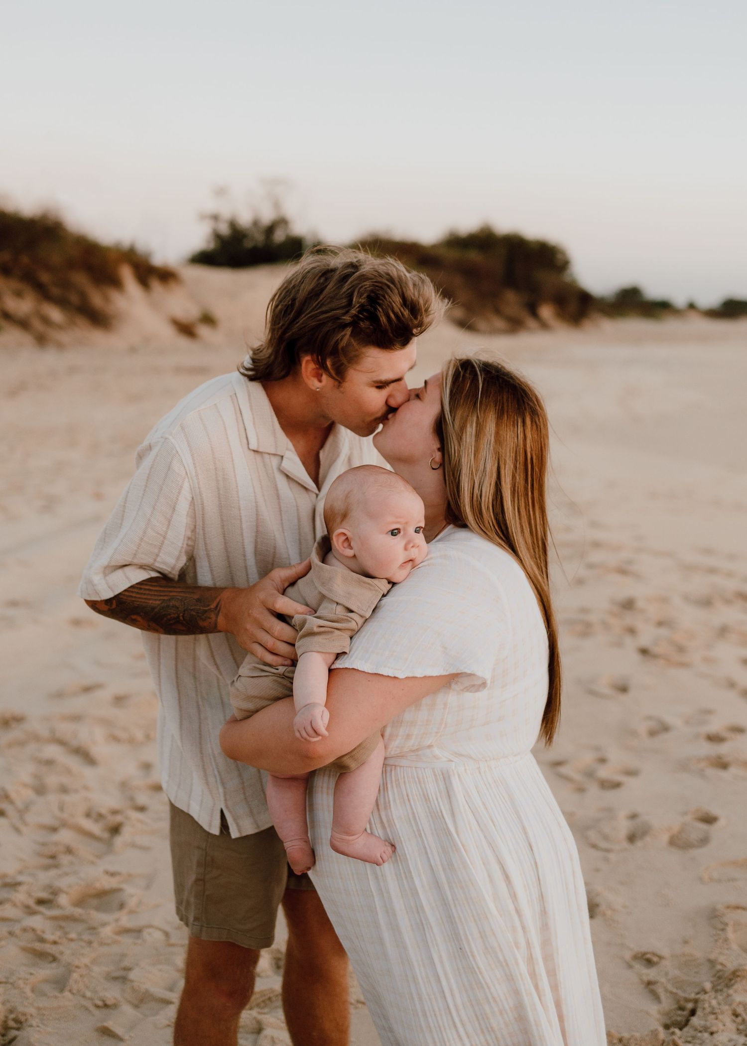 Tender family moment captured on a sandy beach at dusk.