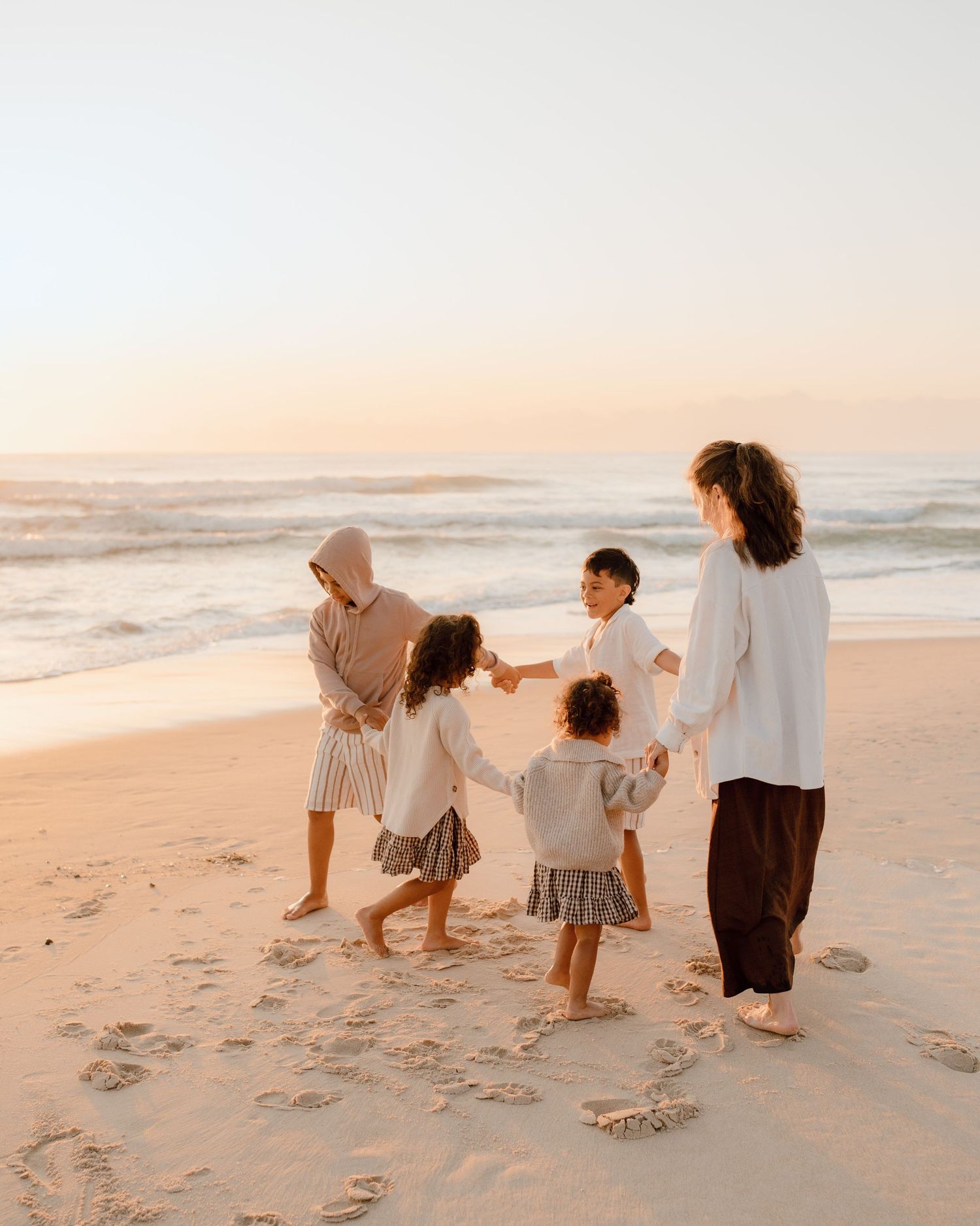 Family walking together on beach at sunset in coordinated neutral outfits.