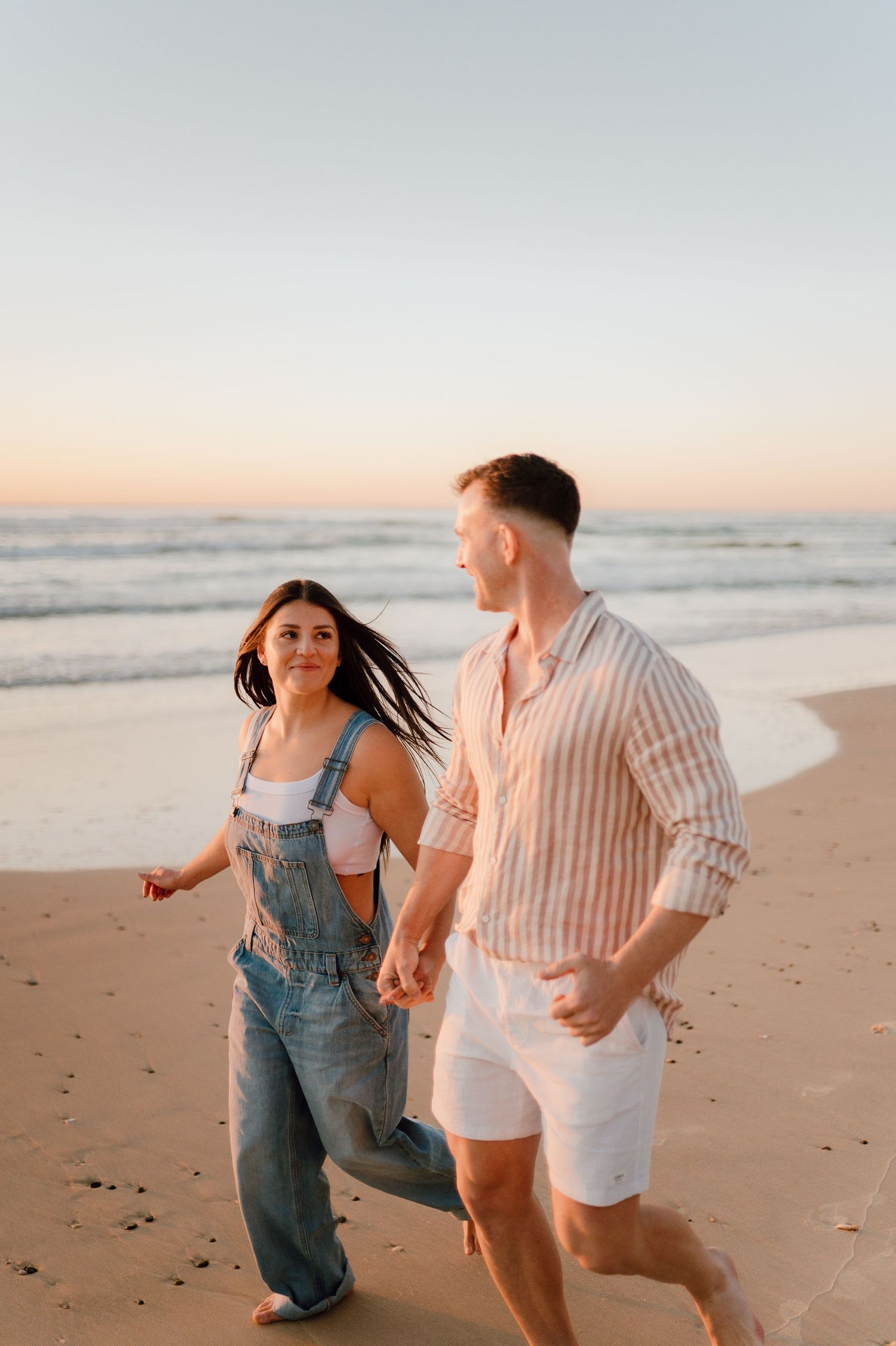 Two people run and play together along the shoreline at sunset.