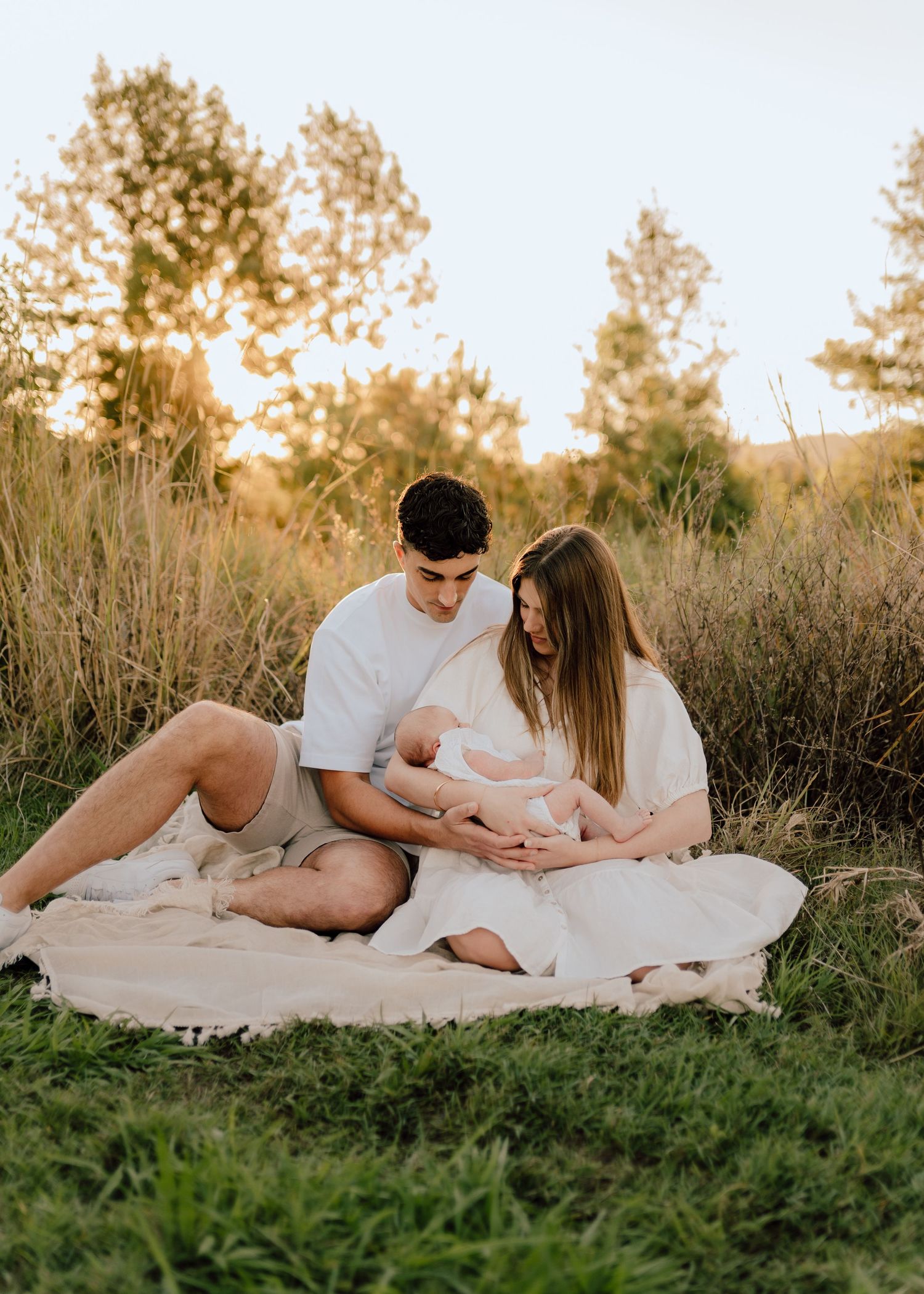 Family relaxing on white blanket in grassy field during golden hour photoshoot.