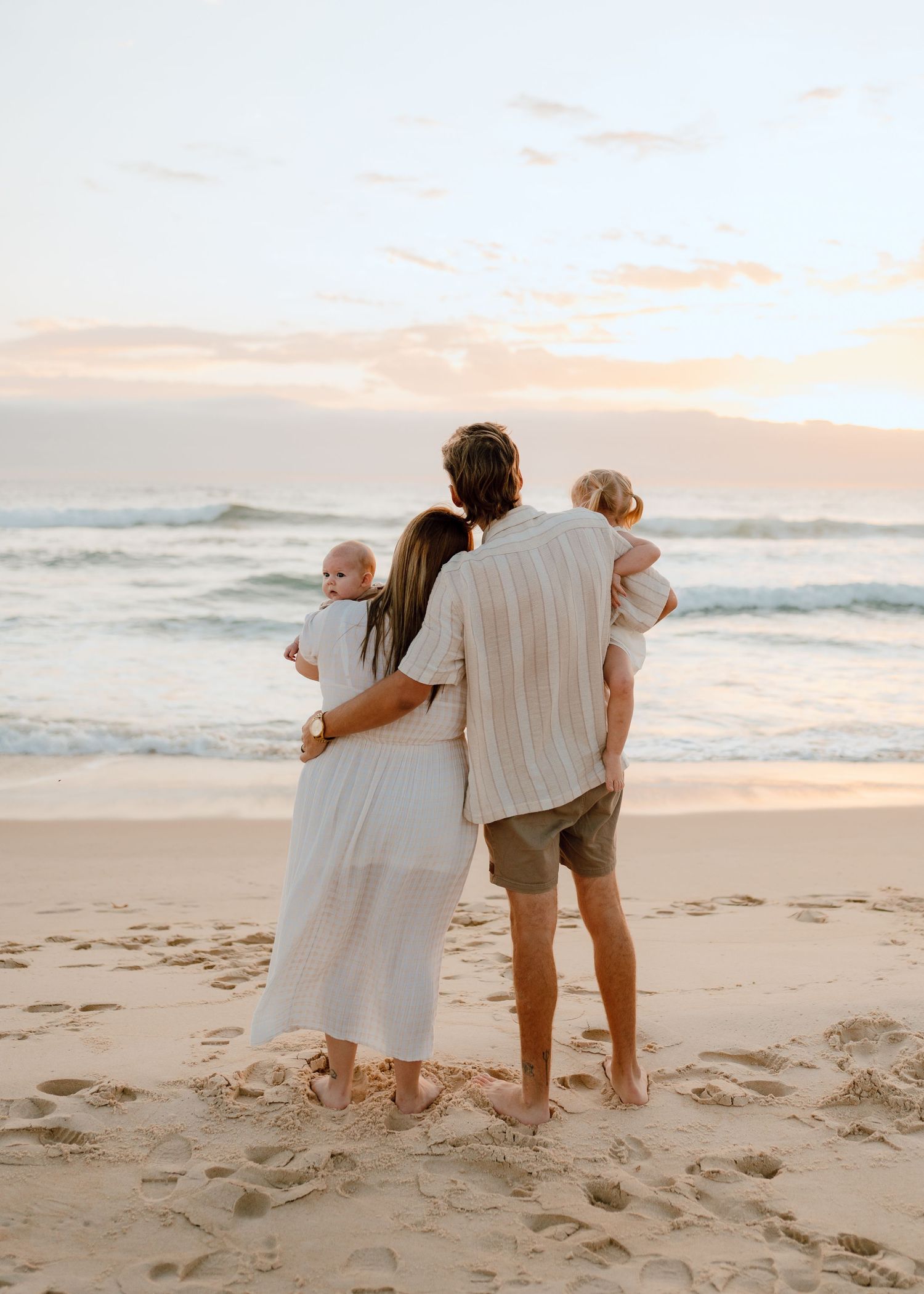 Family in white outfits walking together along a beach at sunset.