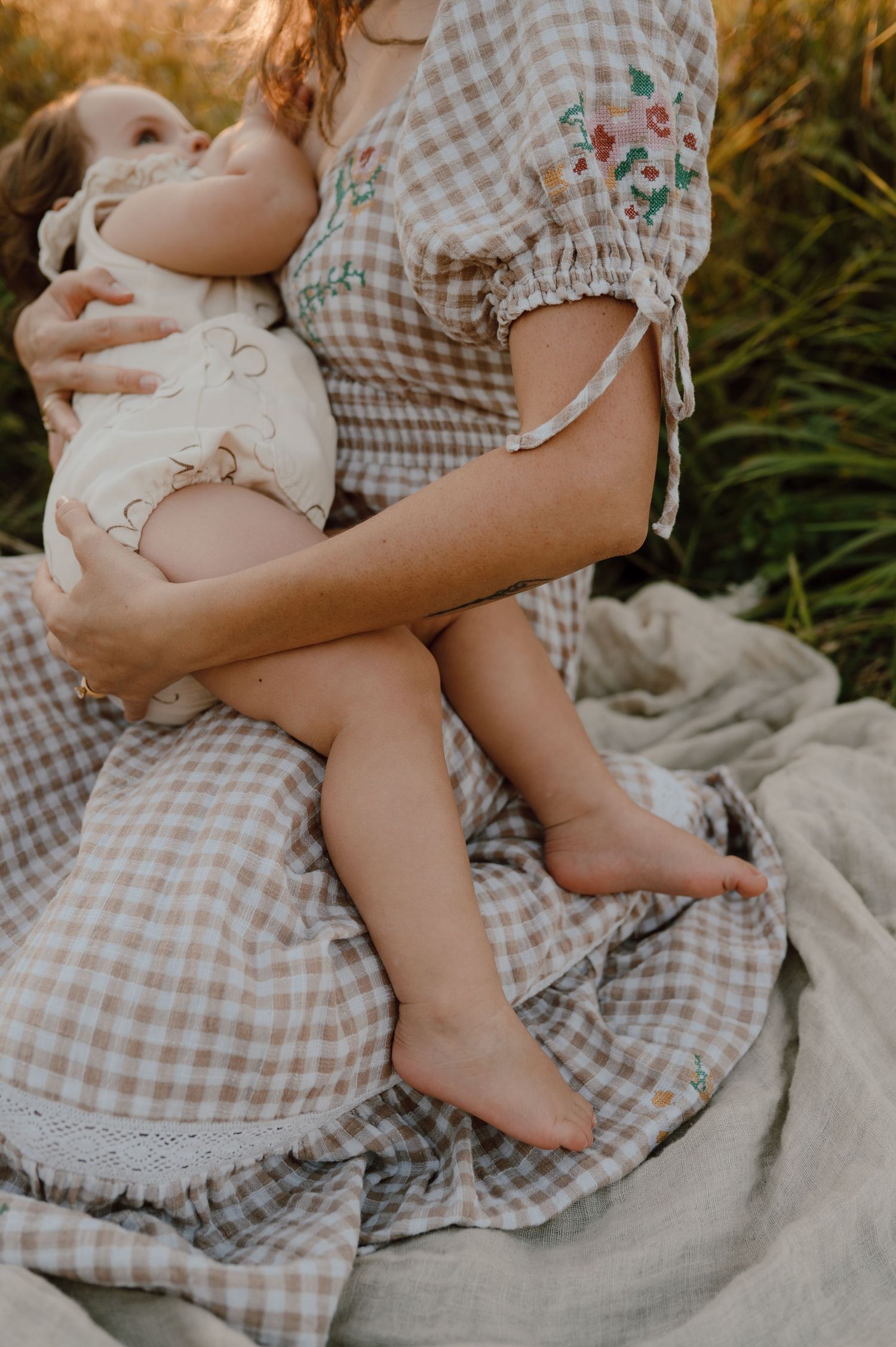 Mother in checkered dress holding baby on white blanket outdoors.